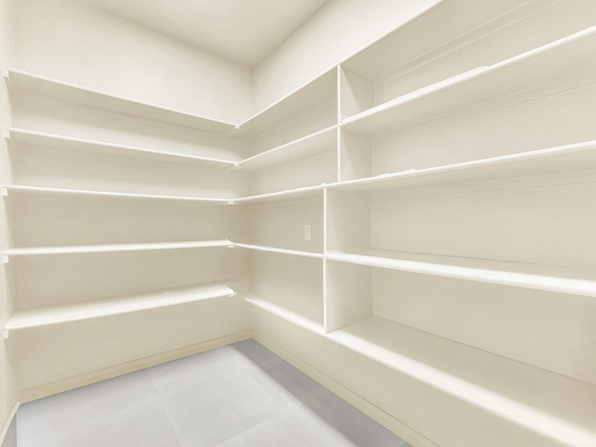 Corner pantry featuring extensive shelving, white painted finishes, and light-toned flooring
