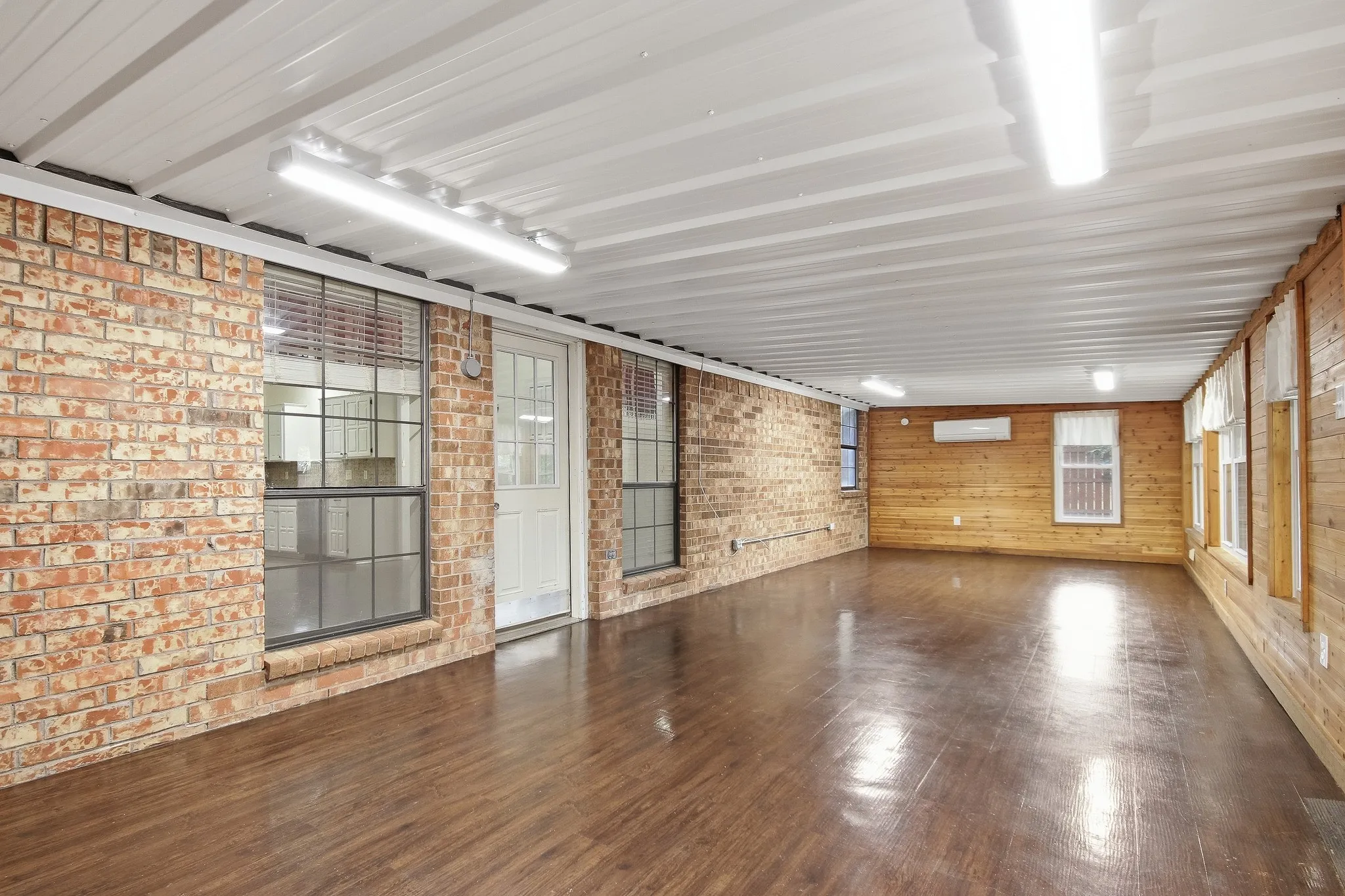 Exposed brick wall, wood-finish flooring, white panel ceiling, white single-panel door, multiple windows with blinds
