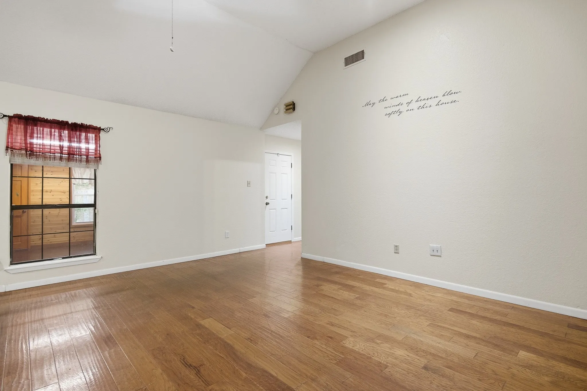 Vaulted ceiling, hardwood flooring, white paneled door, window with dark trim