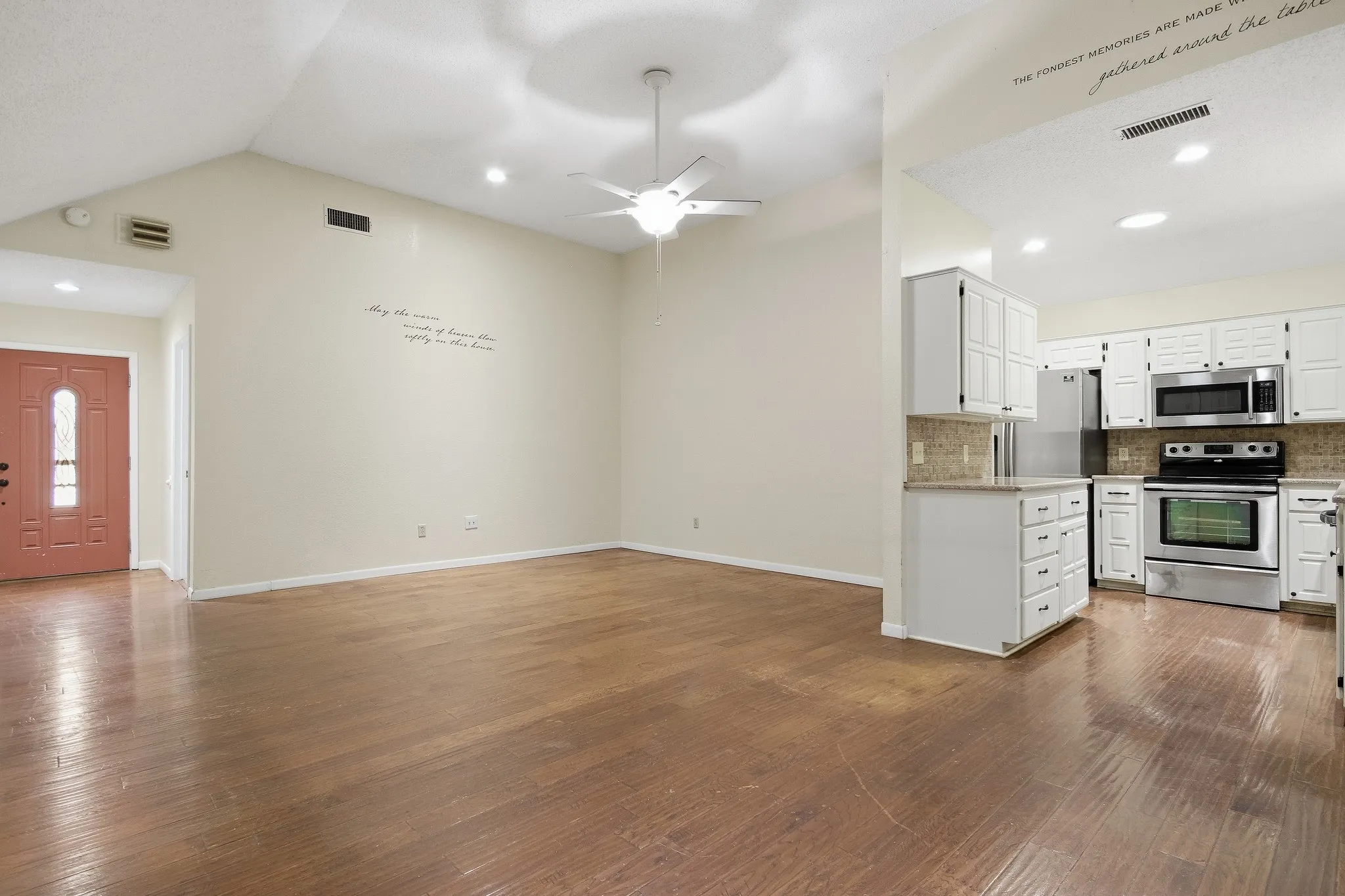 Vaulted ceiling with a ceiling fan, wood-finish flooring, recessed lighting, white kitchen cabinetry, and stainless steel appliances