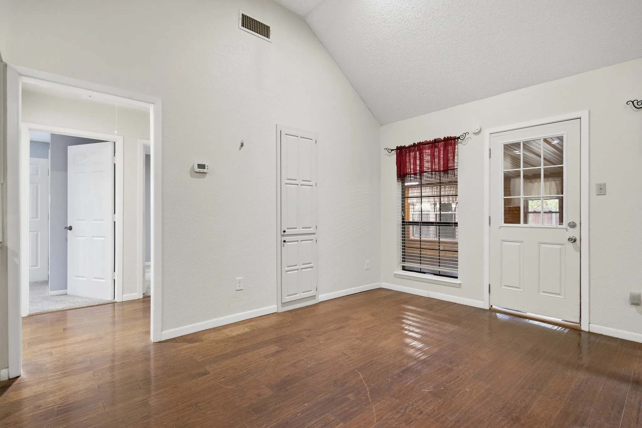 Vaulted ceiling, wood-finish flooring, built-in storage cabinet, window with blinds, and exterior access door with glass panels