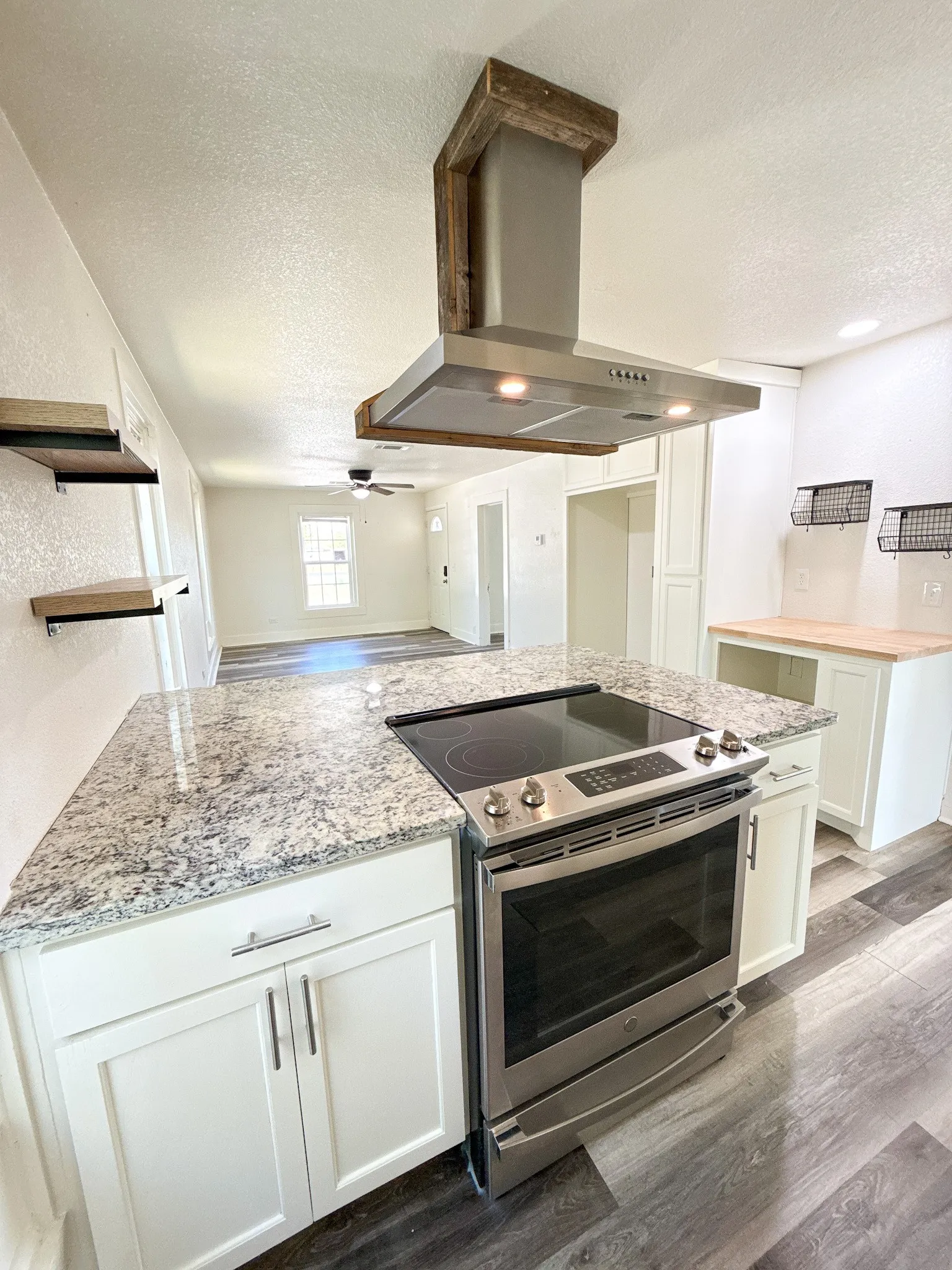Kitchen island featuring a built-in stainless steel range, mottled countertop, and white cabinetry with silver-tone hardware