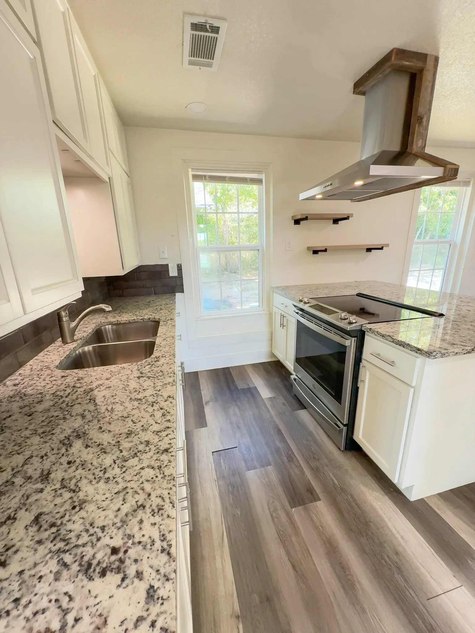 Kitchen featuring granite countertops, stainless steel appliances, white cabinetry, and a wood-wrapped range hood