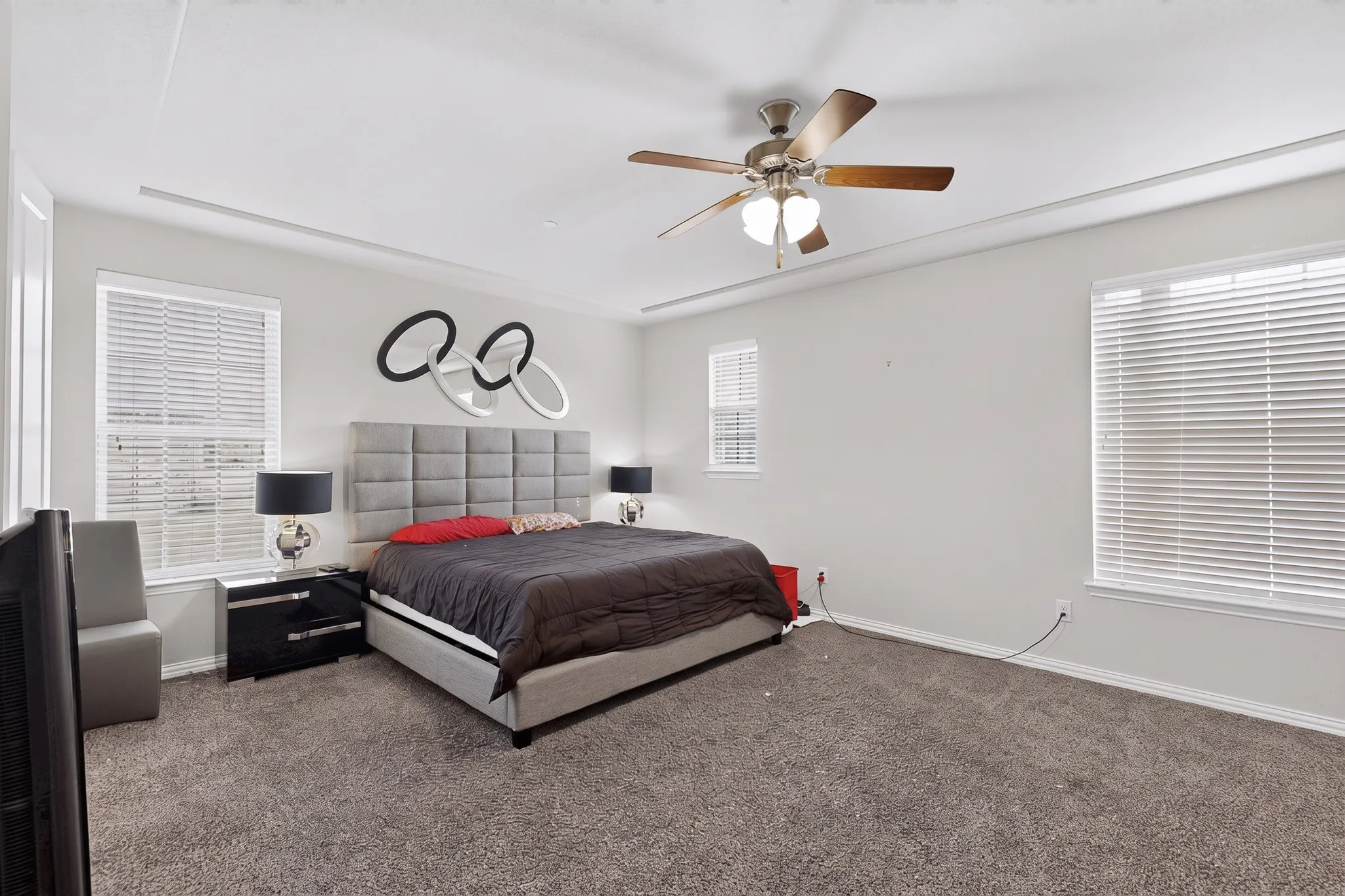 Tray ceiling with crown molding, ceiling fan with integrated lighting, multiple windows with blinds, and carpeted flooring