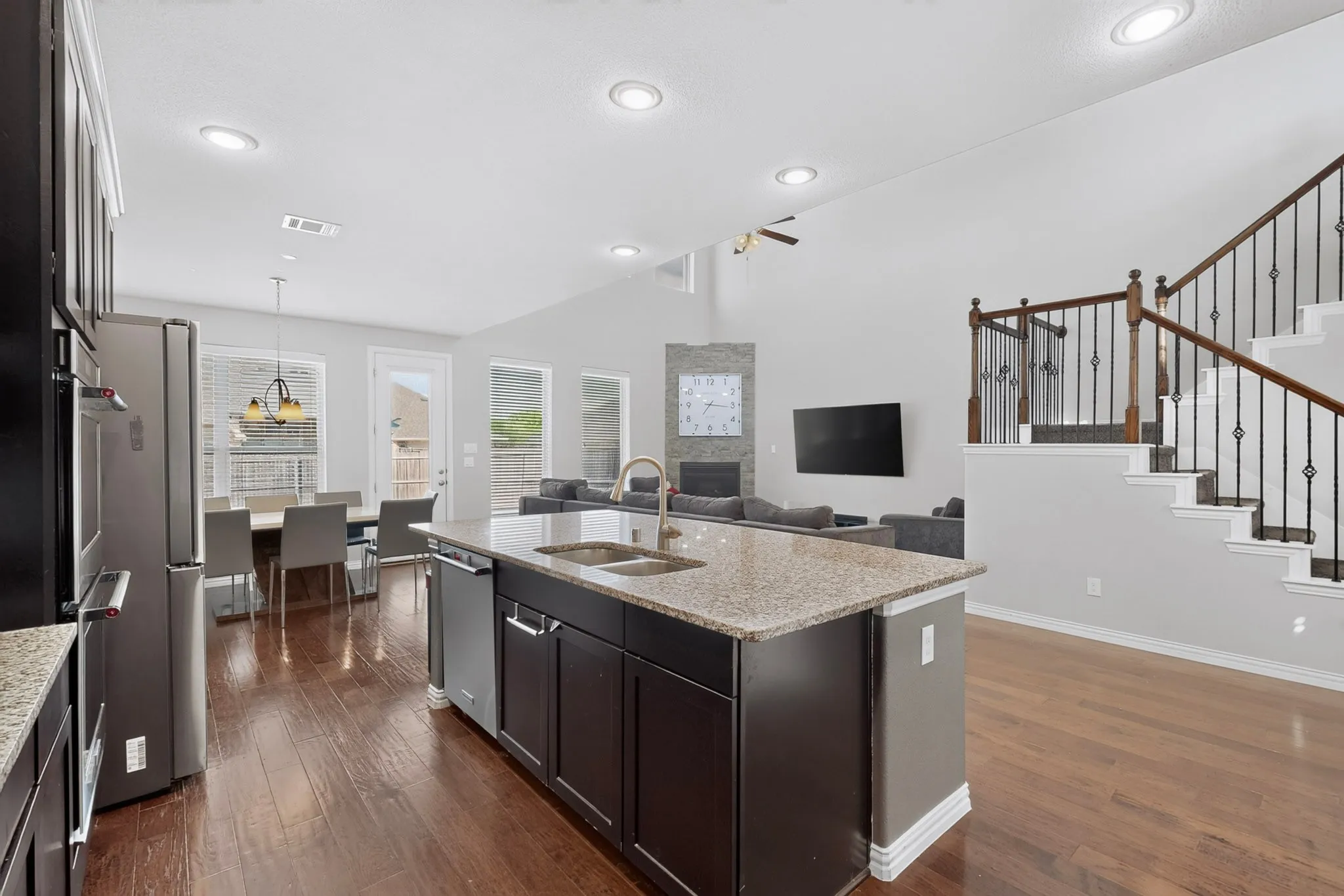 Kitchen island with a granite countertop, stainless steel appliances, wood-finish flooring, vaulted ceilings, and an elegant staircase with wrought iron balusters