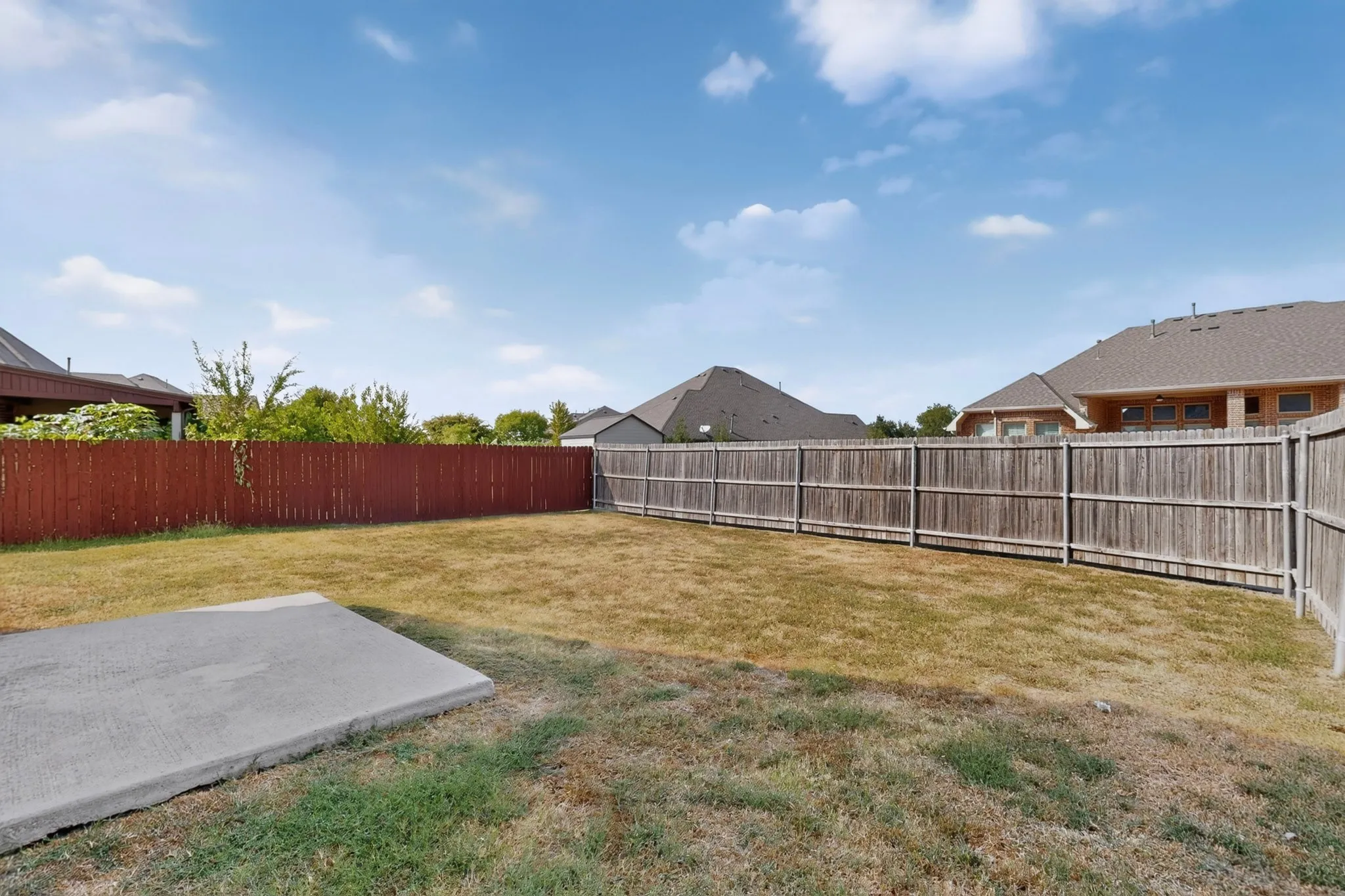 Expansive backyard with a concrete pad, surrounded by a wood privacy fence