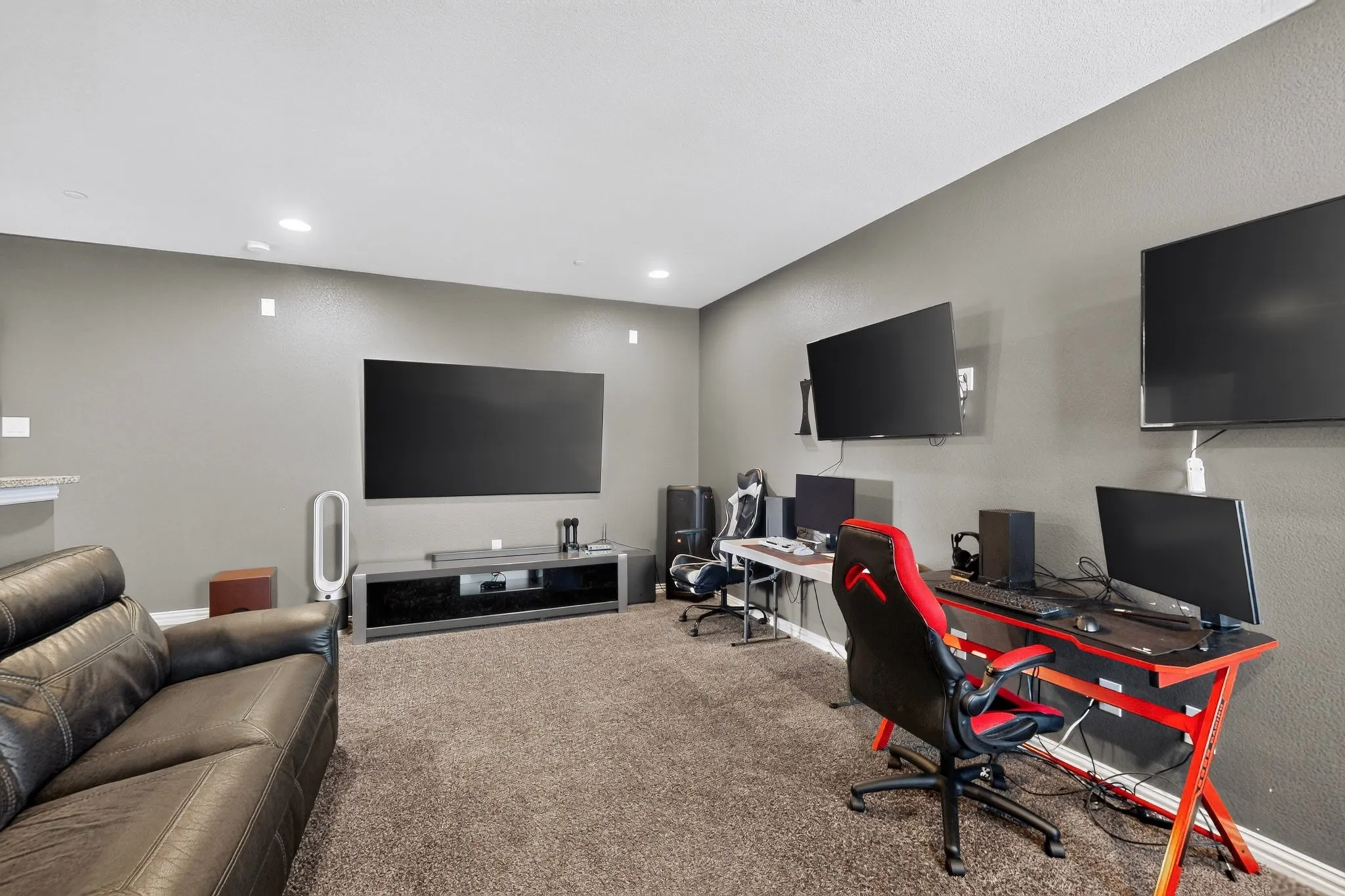 Recessed lighting illuminates a spacious room with wall-mounted televisions and neutral-toned carpeting