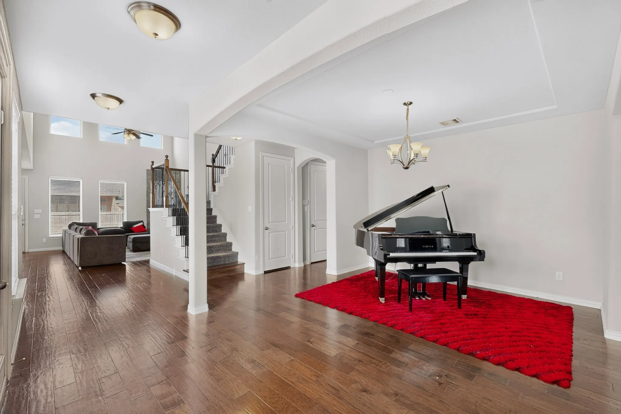 Wood-finish flooring throughout, tray ceiling with chandelier, and a carpeted staircase with wood and metal railing