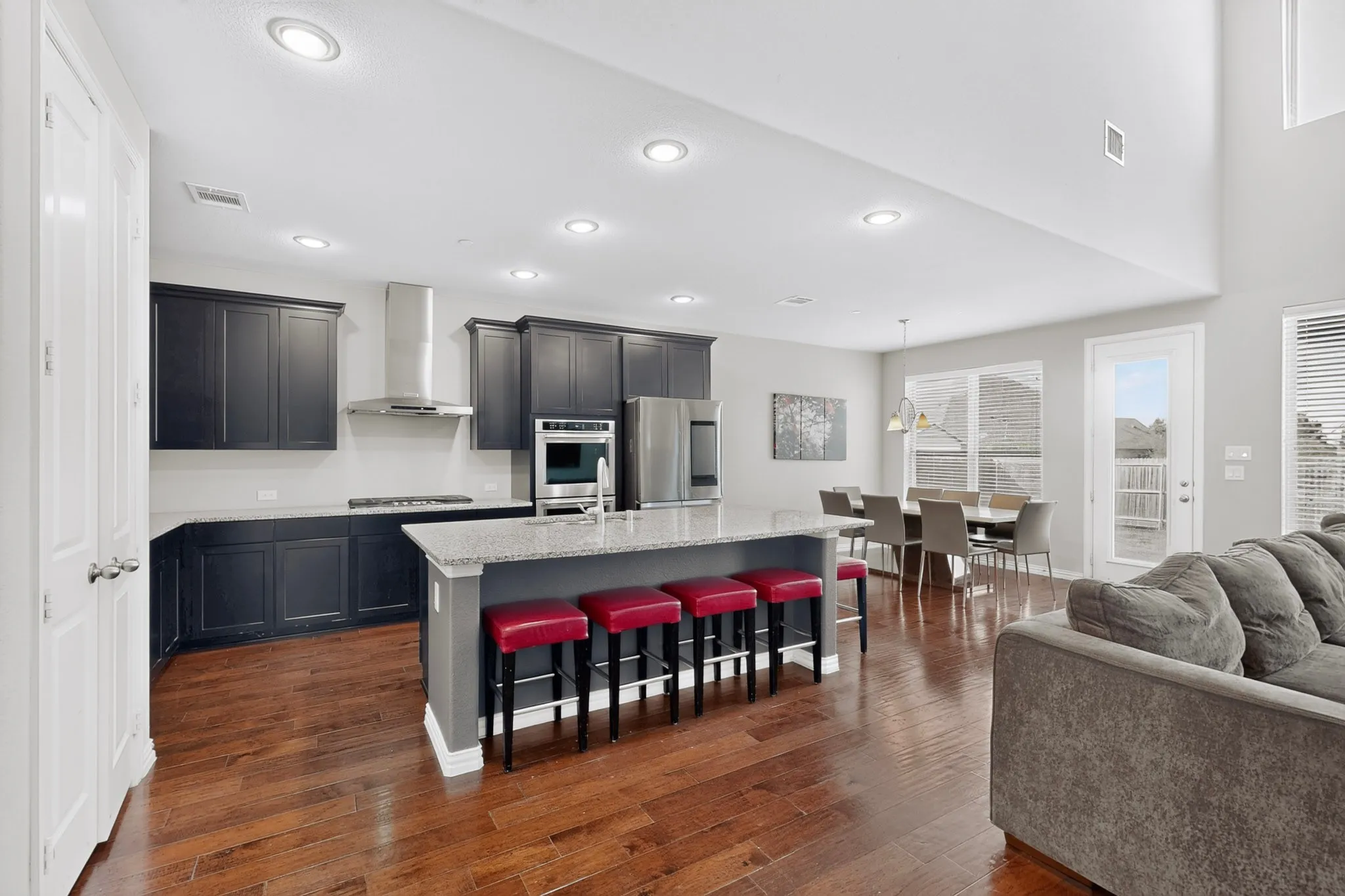 Open-concept living area featuring wood-finish flooring, a kitchen island with stone countertop, stainless steel appliances, and high ceilings