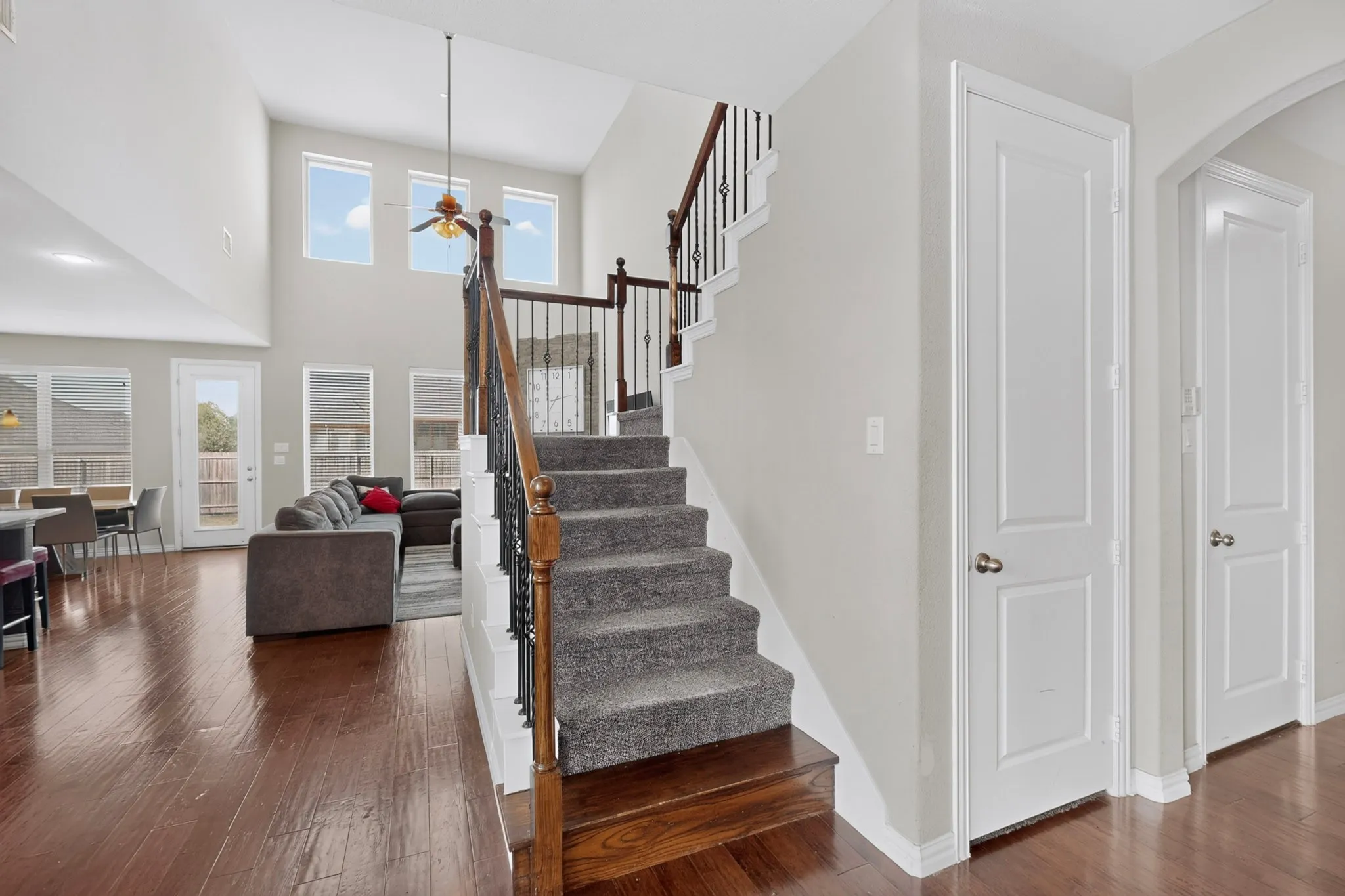 Two-story foyer with high ceilings, wood-finish flooring, and a carpeted staircase featuring a wood handrail and iron balusters