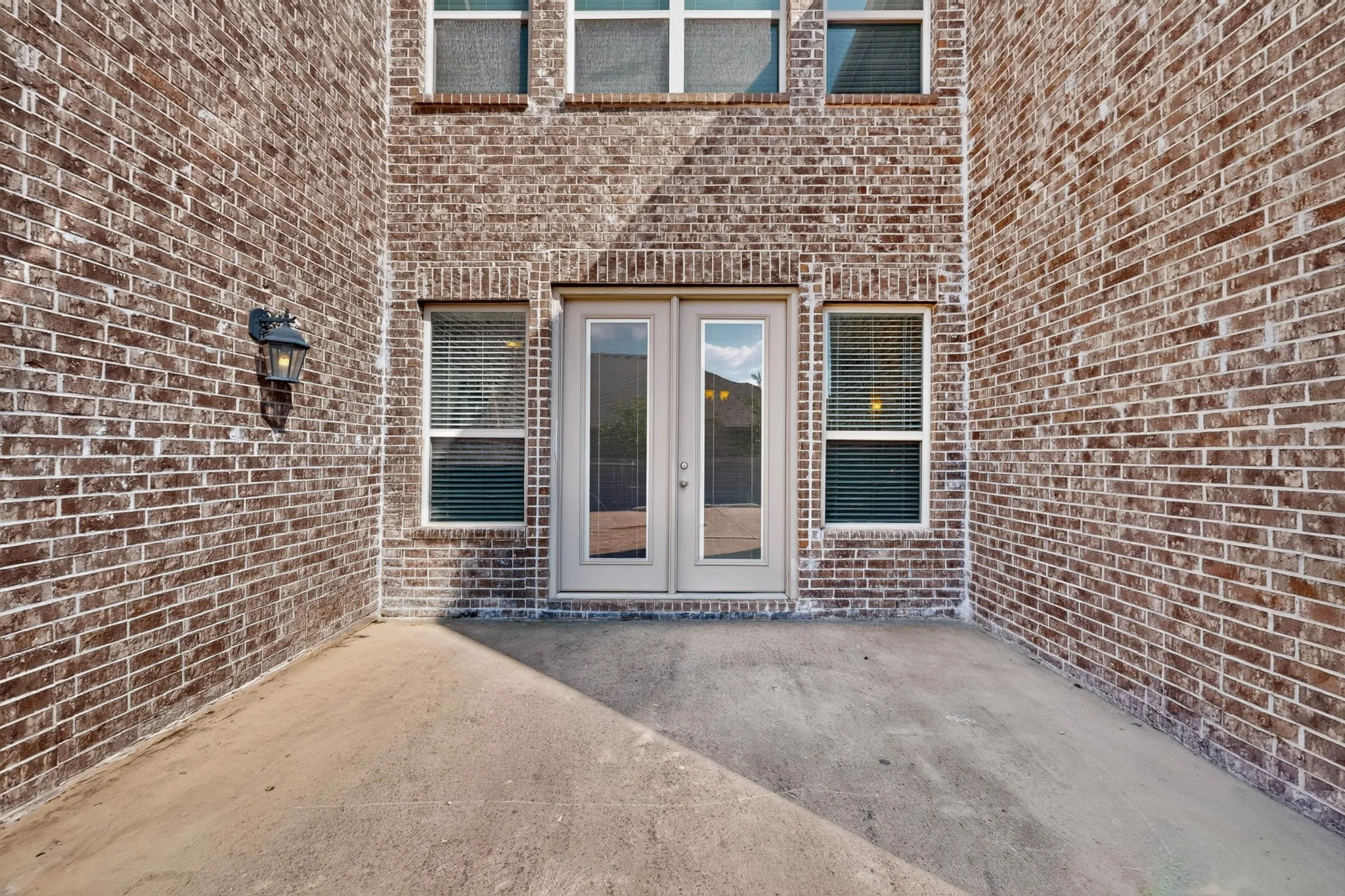 Brick exterior with a concrete patio, double French doors, and an exterior wall light fixture