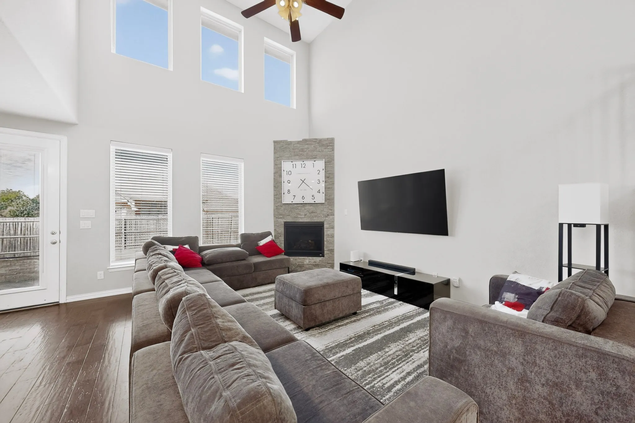 20 foot Vaulted ceiling with a ceiling fan, dark wood-finish flooring, stone-clad fireplace, and transom windows