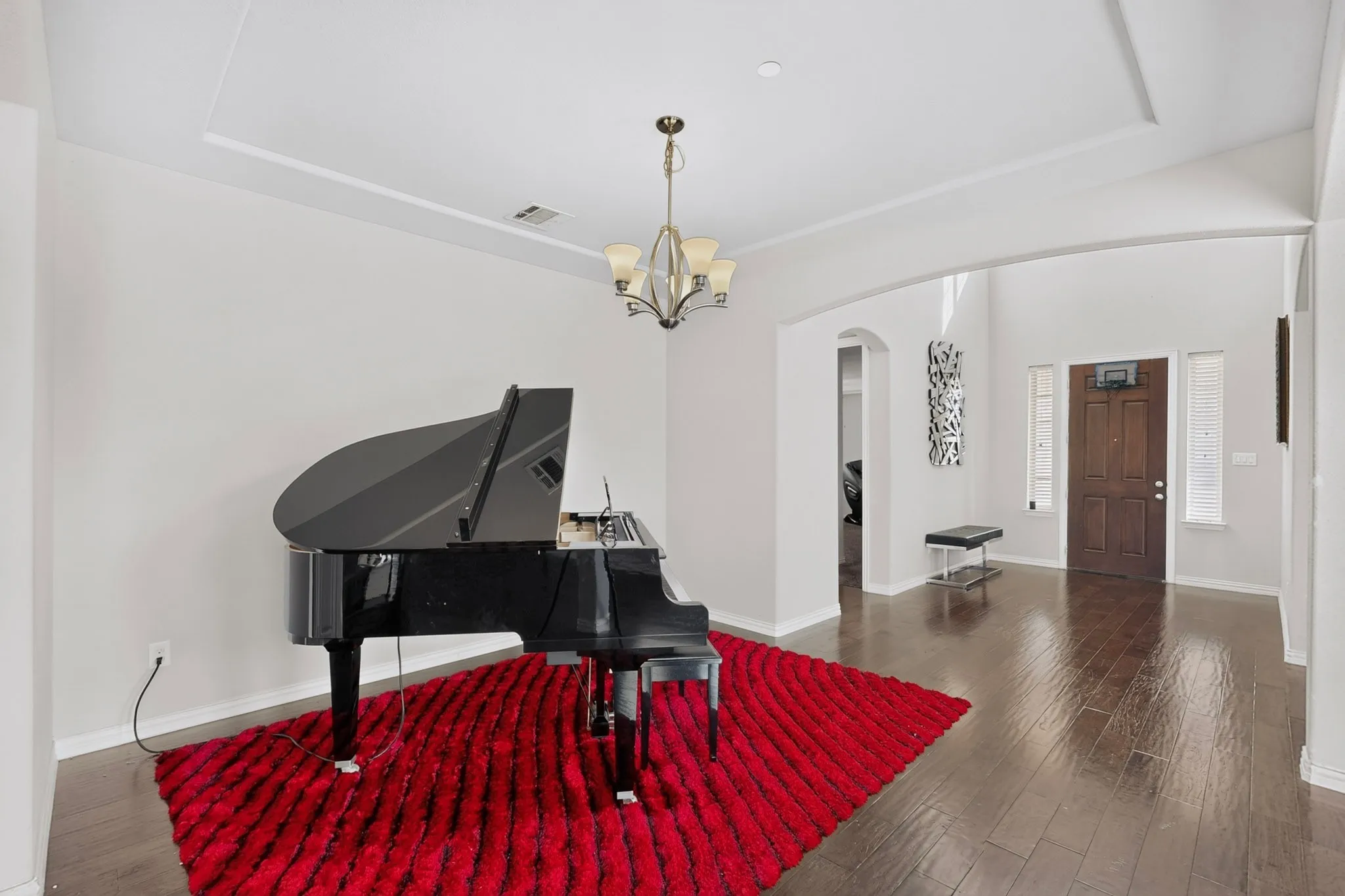 Tray ceiling with a decorative chandelier, dark wood-finish flooring, and arched entryway