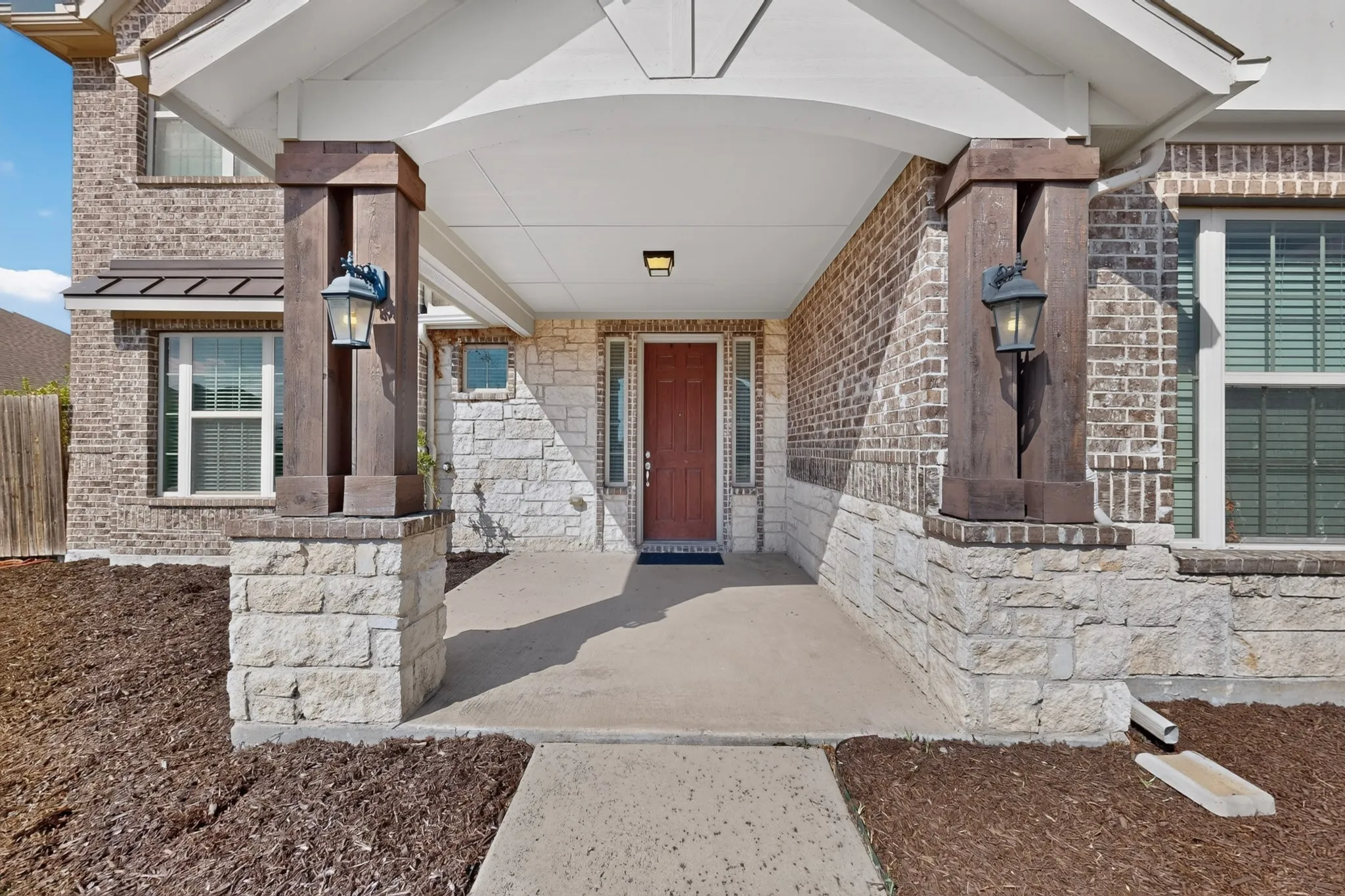 Brick and stone facade, covered entry, and a solid wood-finish front door