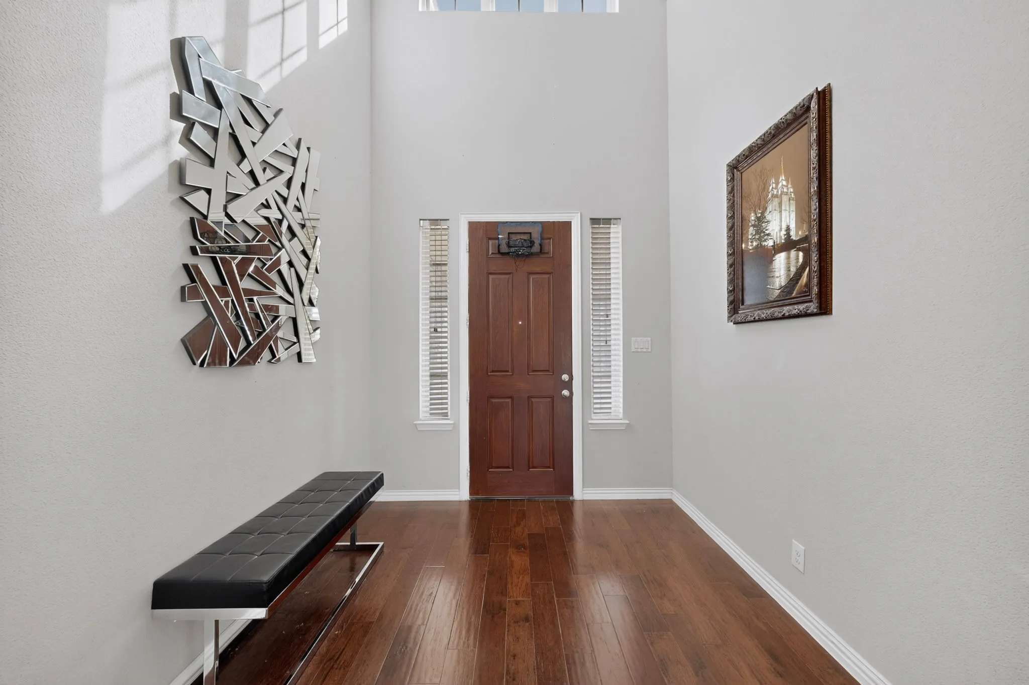 Double-height entryway featuring a dark wood-paneled door with transom window and sidelights, and rich wood-finish flooring