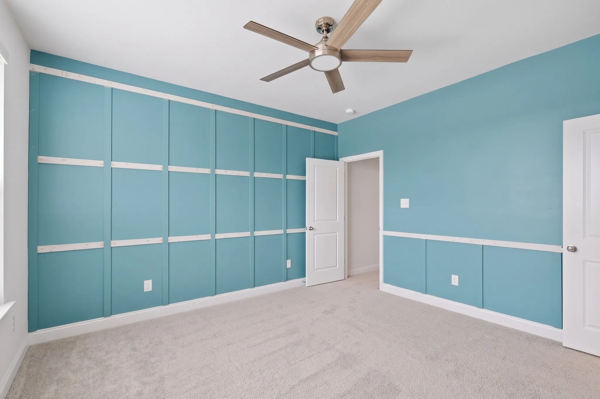 Accent wall with grid paneling, neutral carpet, ceiling fan with brushed nickel finish, and white paneled doors