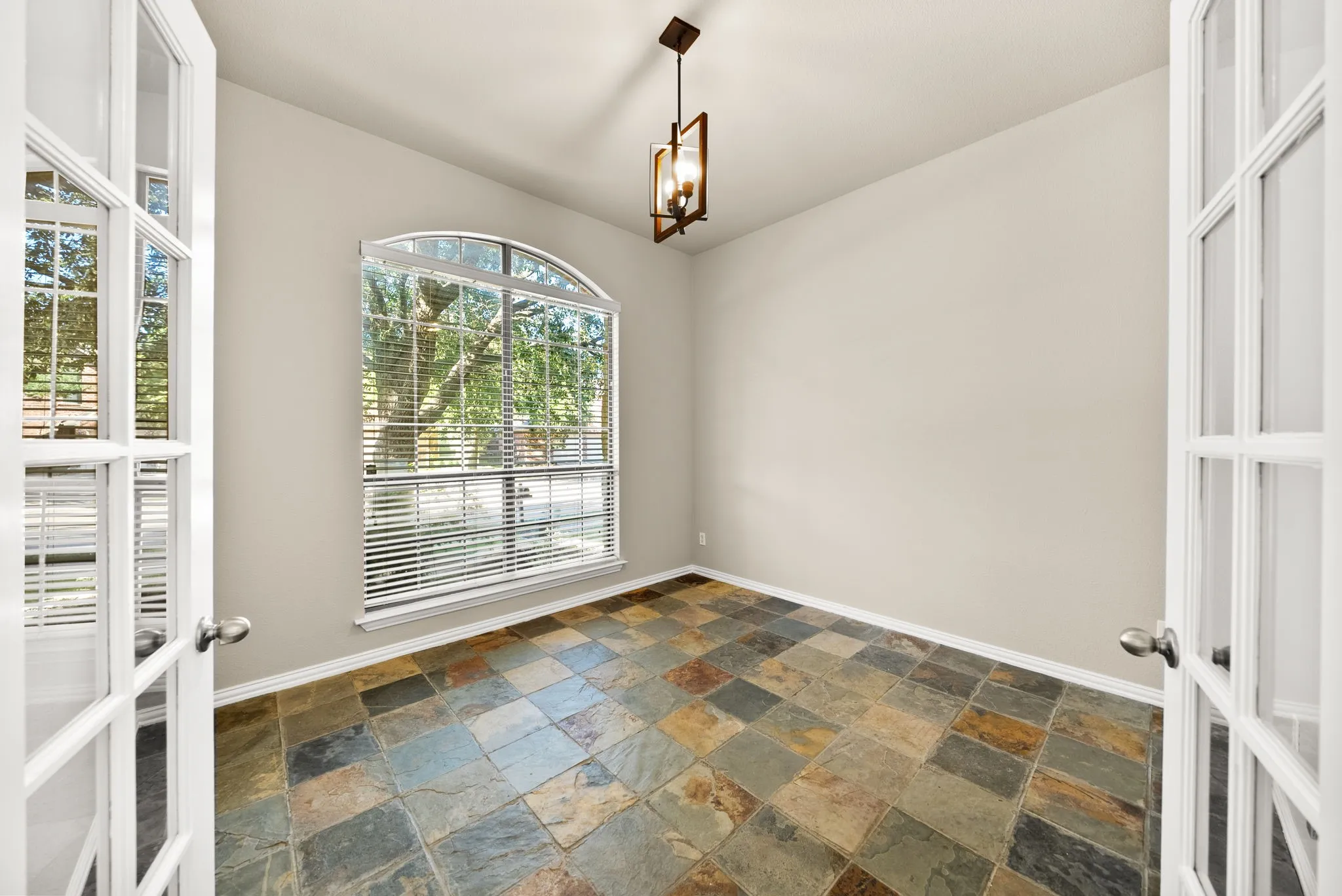 Arched picture window, double French doors, multicolor slate tile flooring, and a ceiling-mounted light fixture