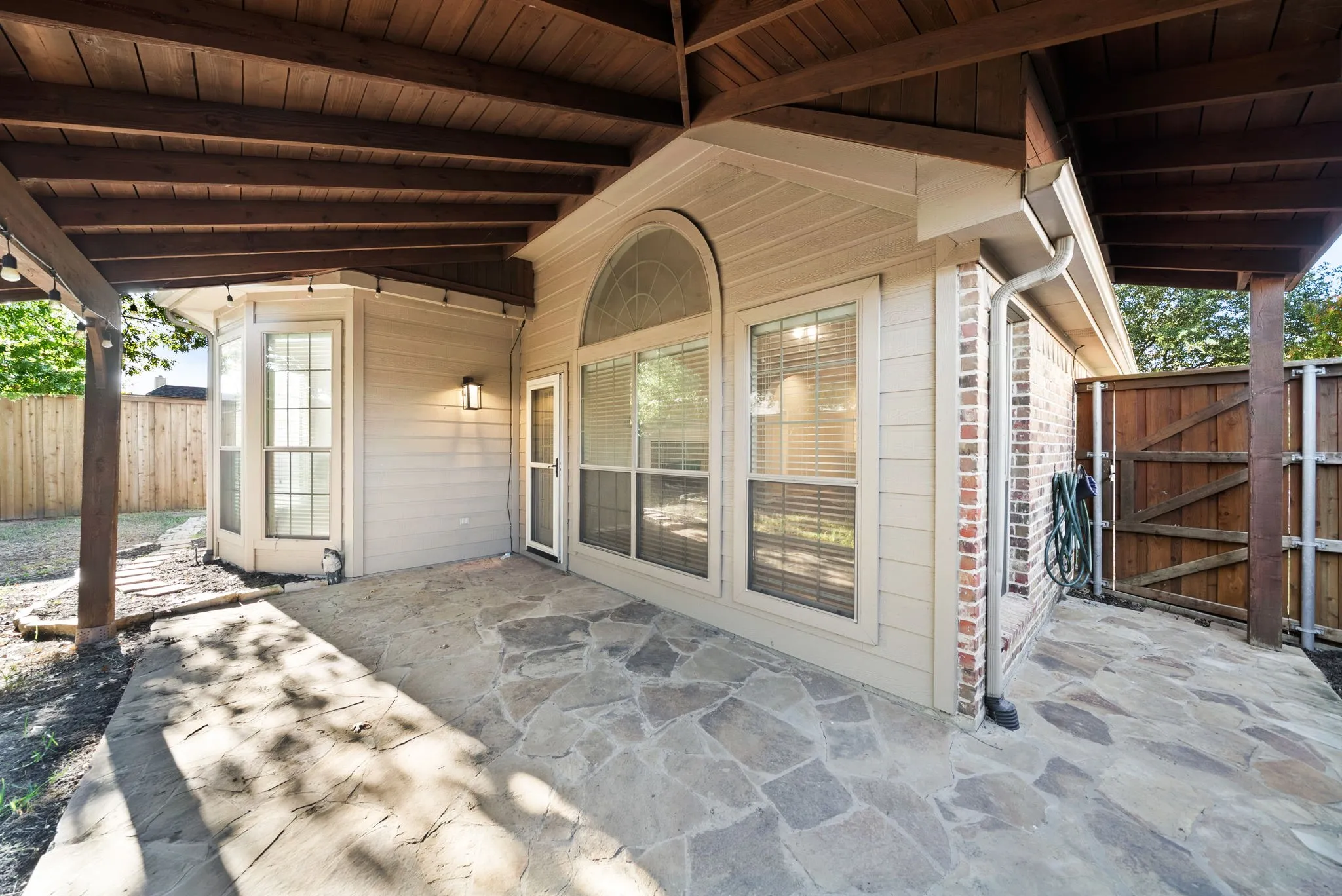 Covered patio featuring flagstone paving, wood-plank ceiling, and exterior lighting