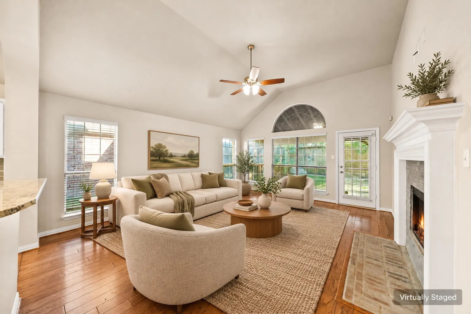 Vaulted ceiling with ceiling fan, hardwood flooring, fireplace with mantel, multiple windows, and a glass-paneled exterior door