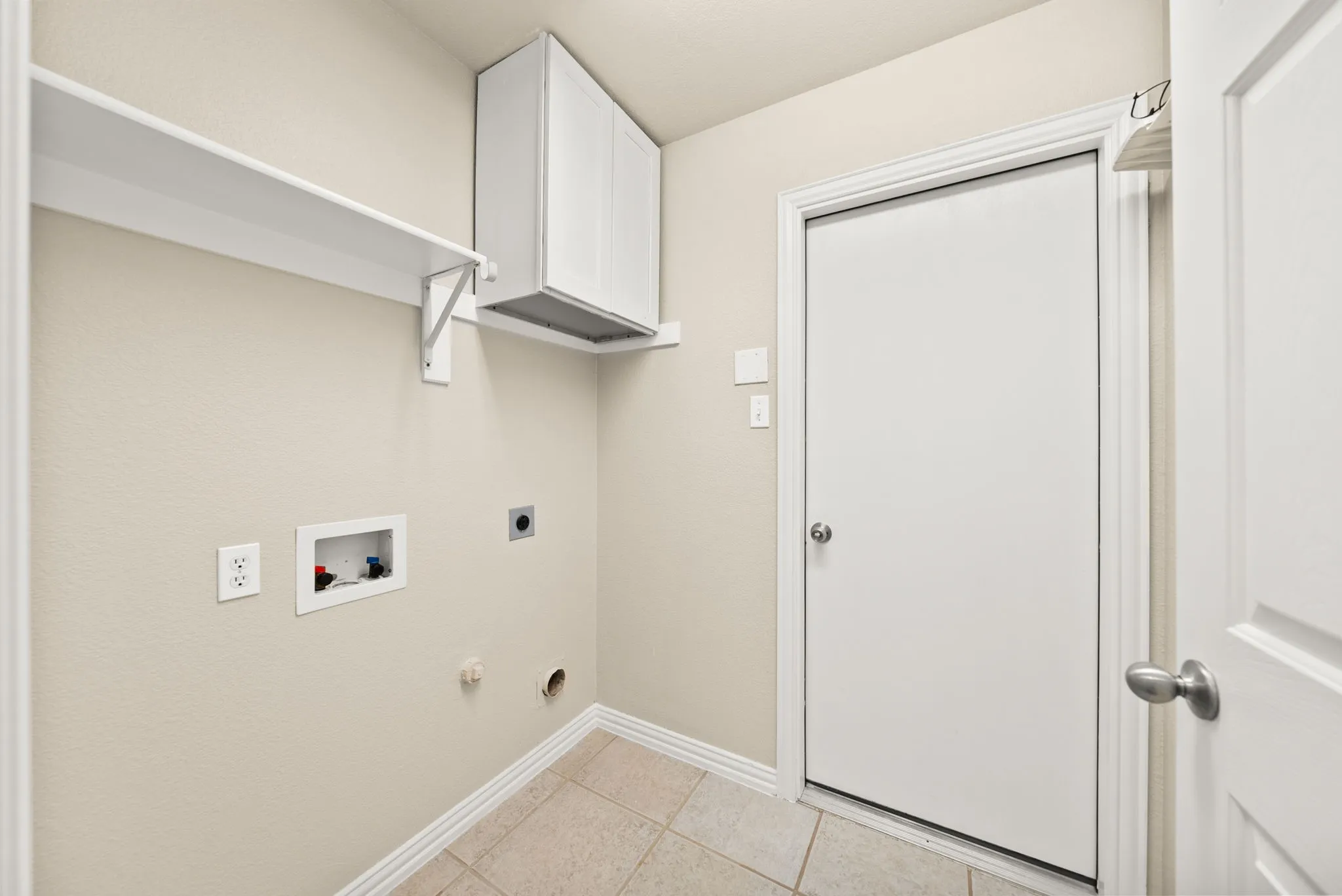 Laundry area with tiled flooring, wall-mounted shelving, and upper cabinetry