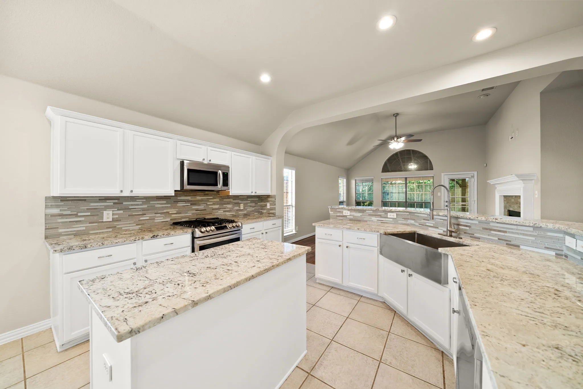 Kitchen featuring white cabinetry, light-toned countertops, a stainless steel farmhouse sink, and a tiled backsplash