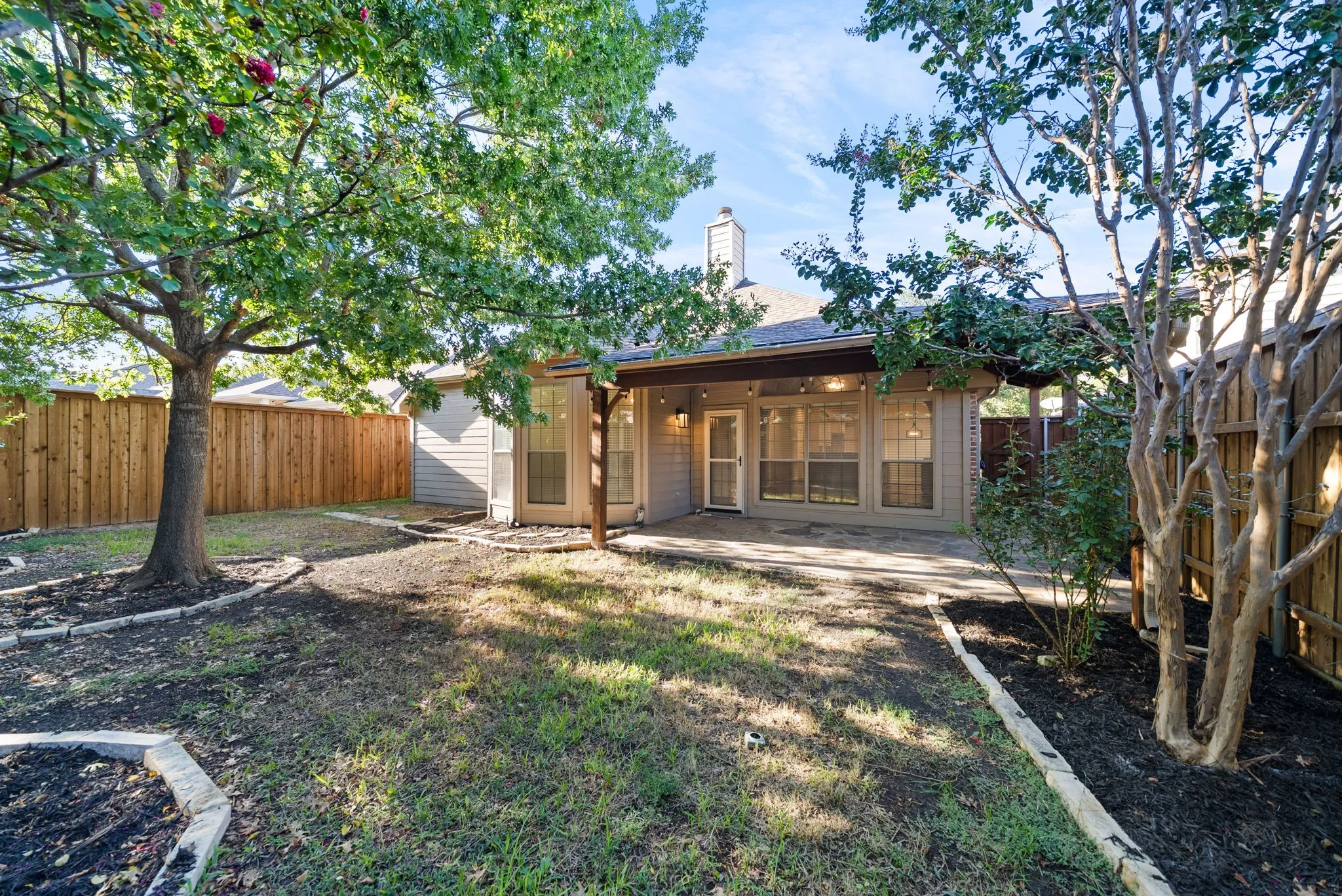 Expansive backyard featuring a covered patio, privacy fencing, mature trees, and landscaping beds