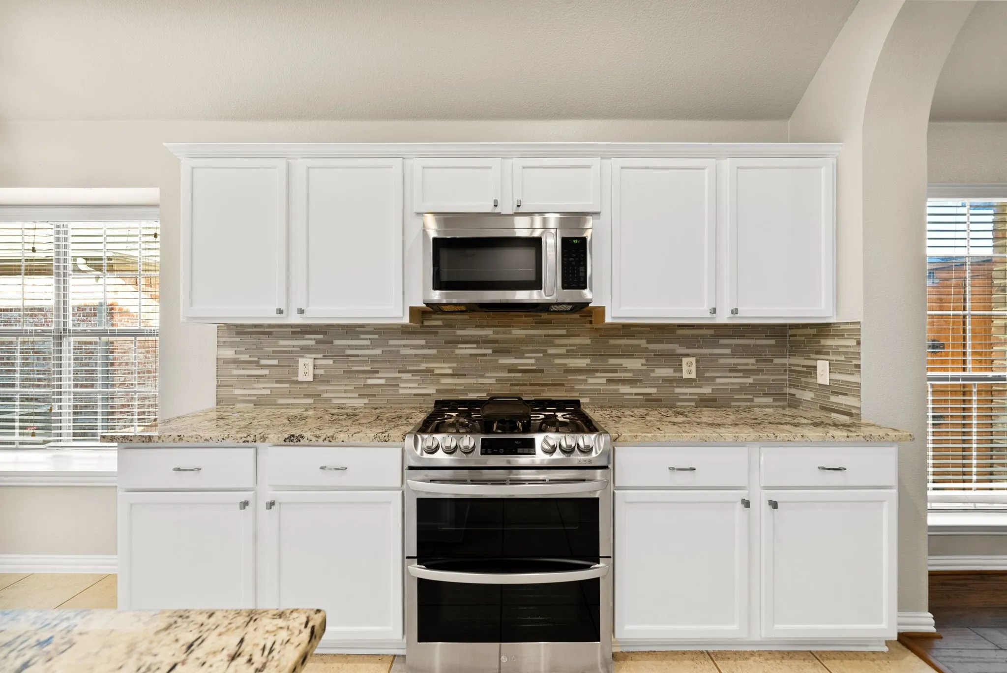 White cabinetry, stainless steel oven with gas range, stainless steel microwave, stone countertops, and a tiled backsplash