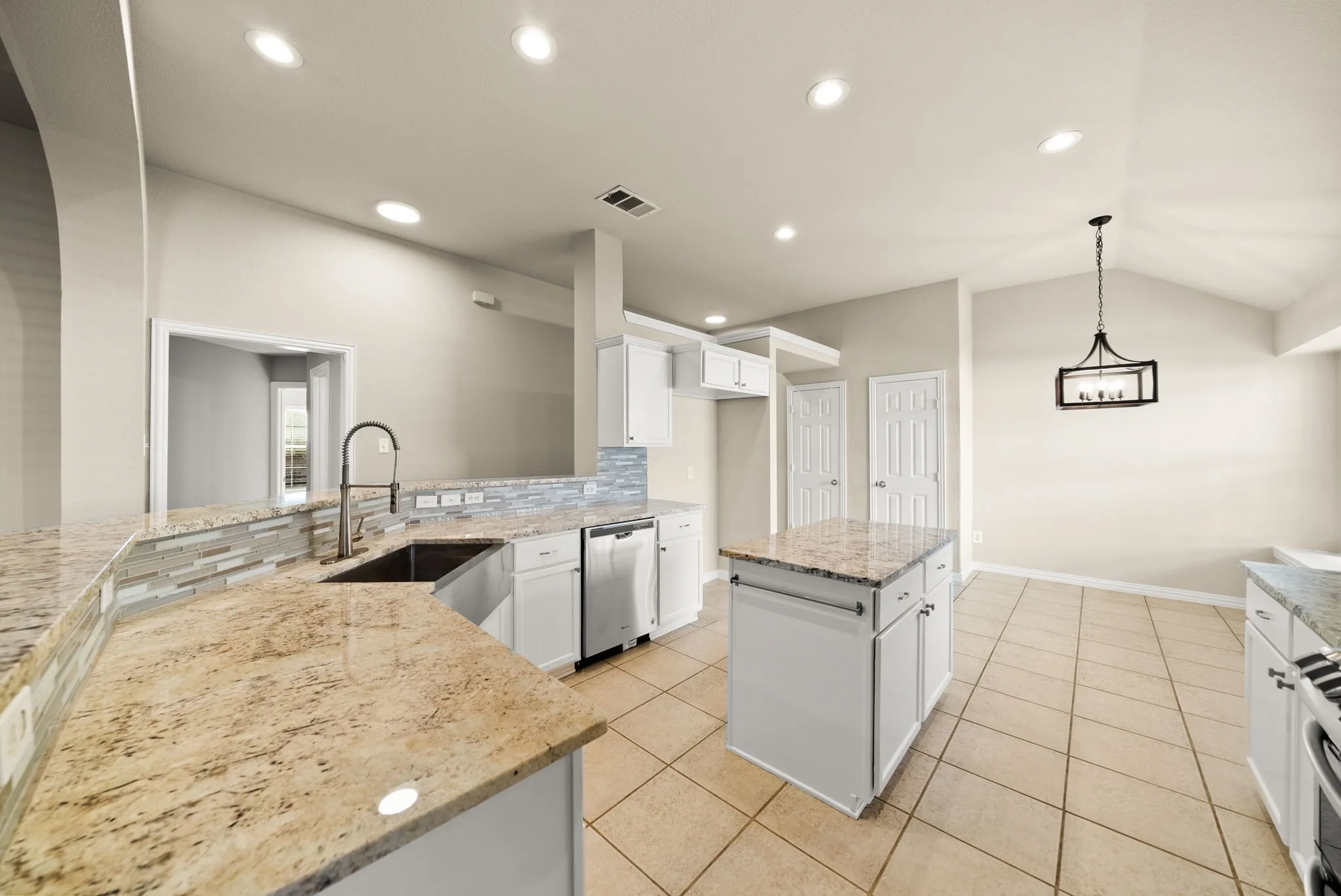 Spacious kitchen featuring granite countertops, stainless steel appliances, a large center island with prep space, tile flooring, recessed lighting, and a pendant fixture overhead