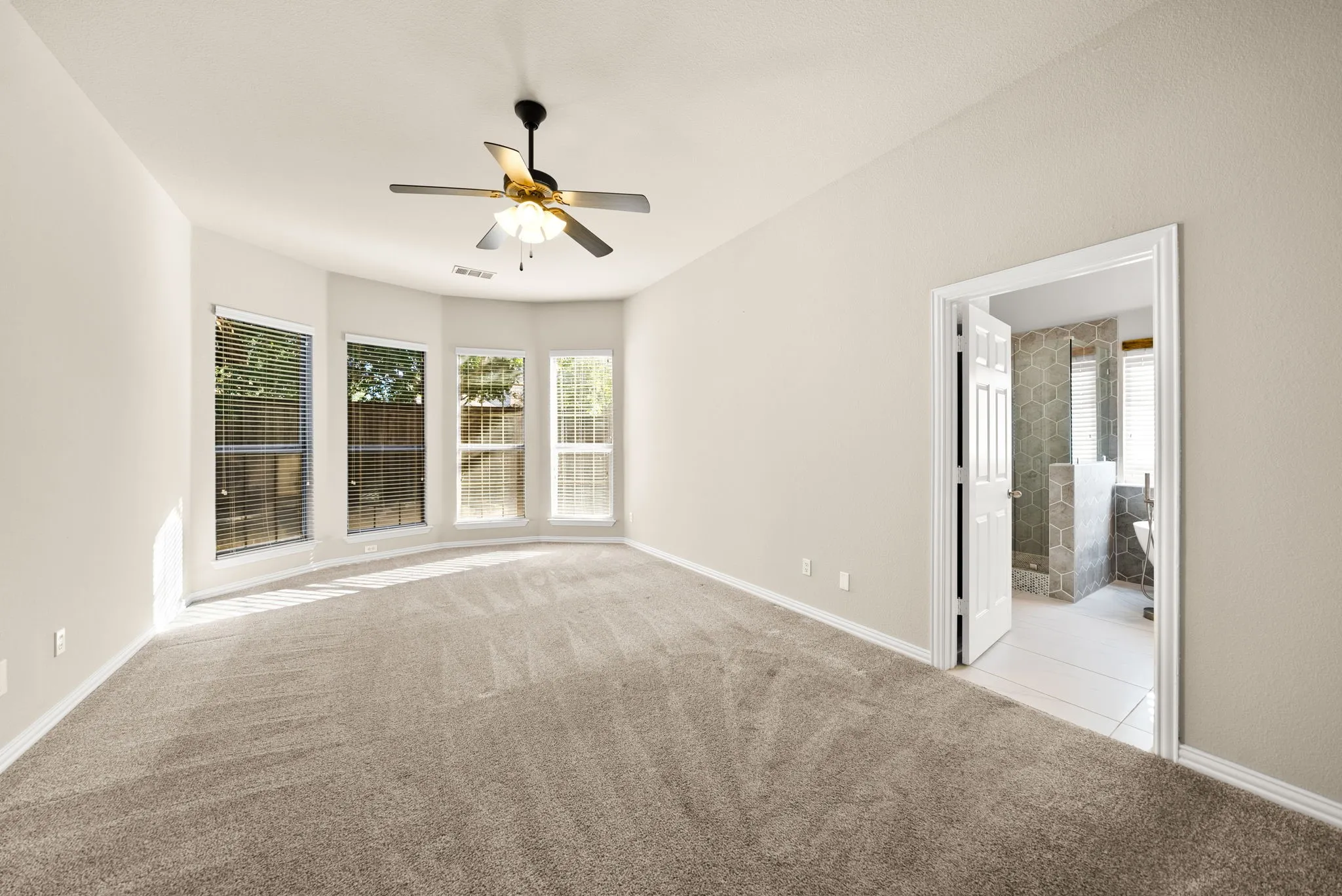 Spacious room featuring neutral carpeting, a ceiling fan, and a bay window configuration with multiple windows