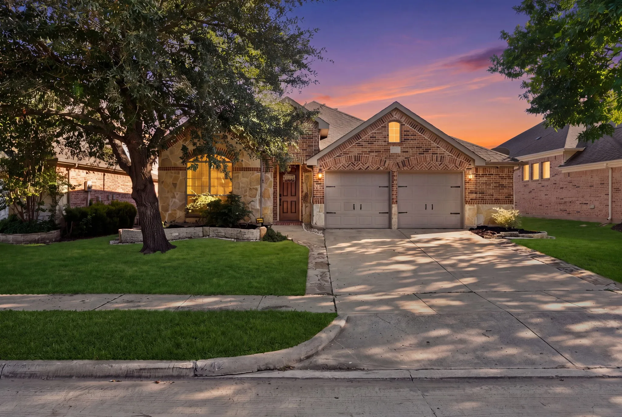 Brick and stone exterior with arched window, two-car garage, concrete driveway, and manicured landscaping