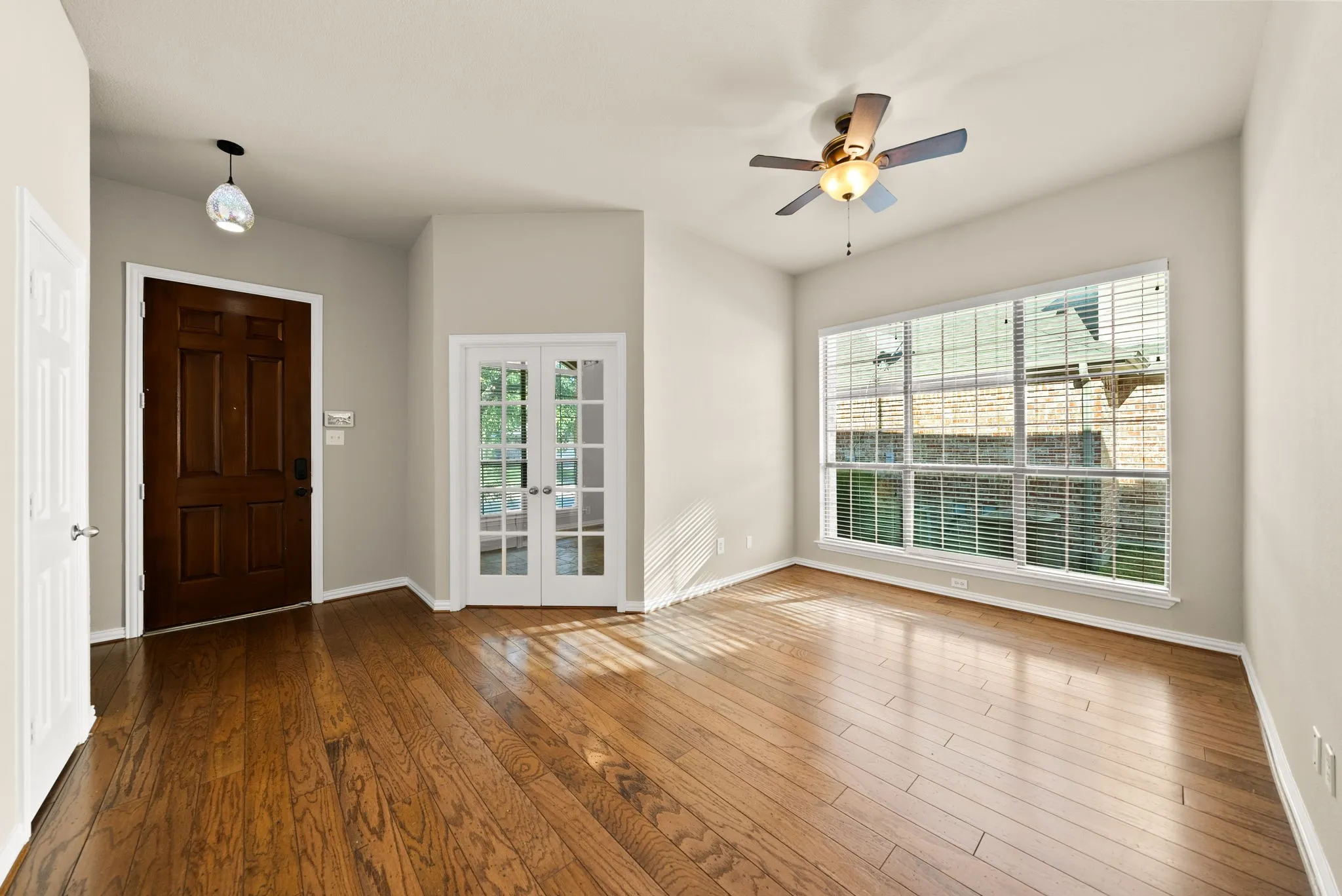 Wood-finish flooring throughout, vaulted ceiling, white frame french doors, large multipane window, and a ceiling fan with integrated lighting