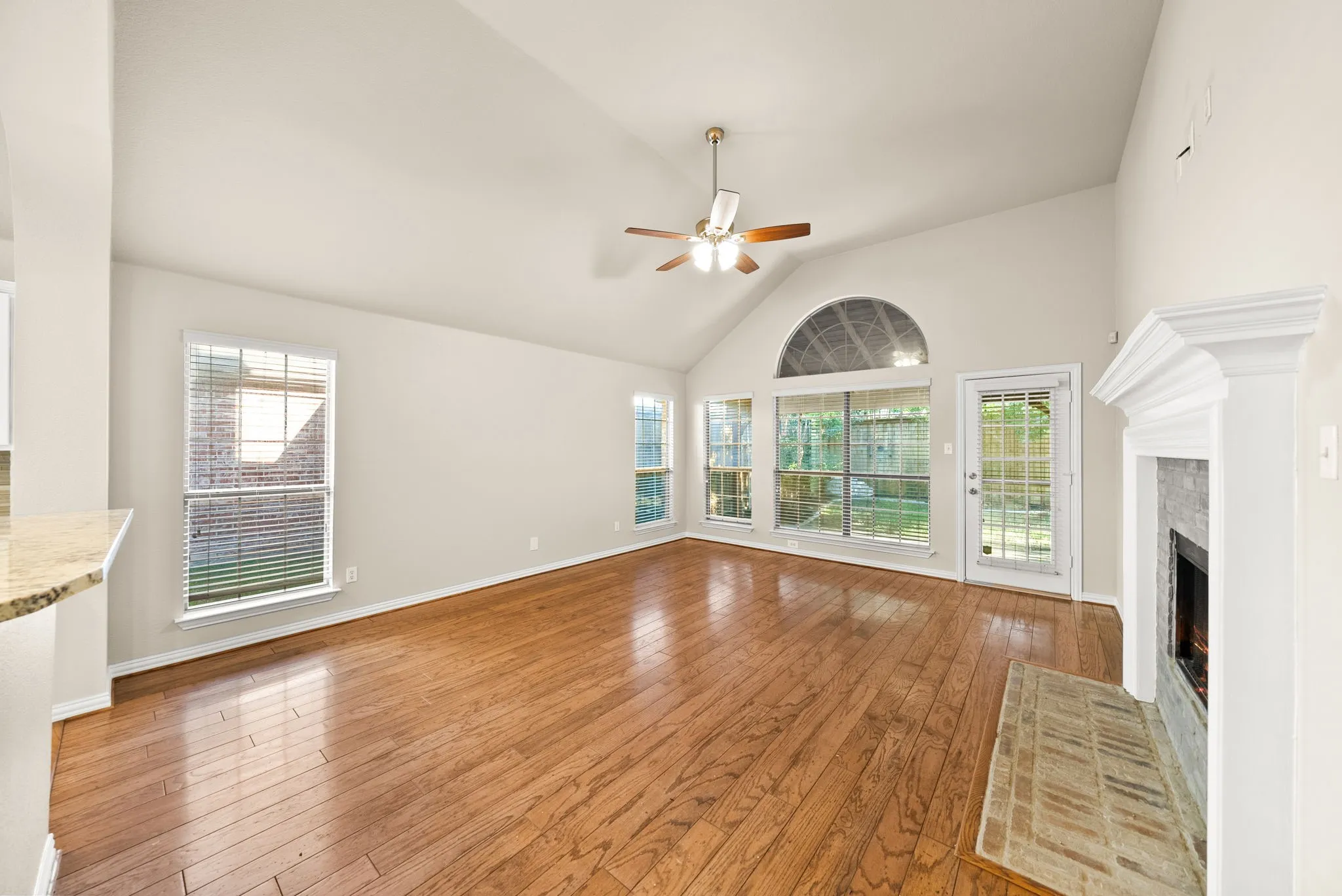 Vaulted ceiling with a ceiling fan, wood-finish flooring, multiple windows, fireplace with a tiled hearth, and a glass-paneled exterior door