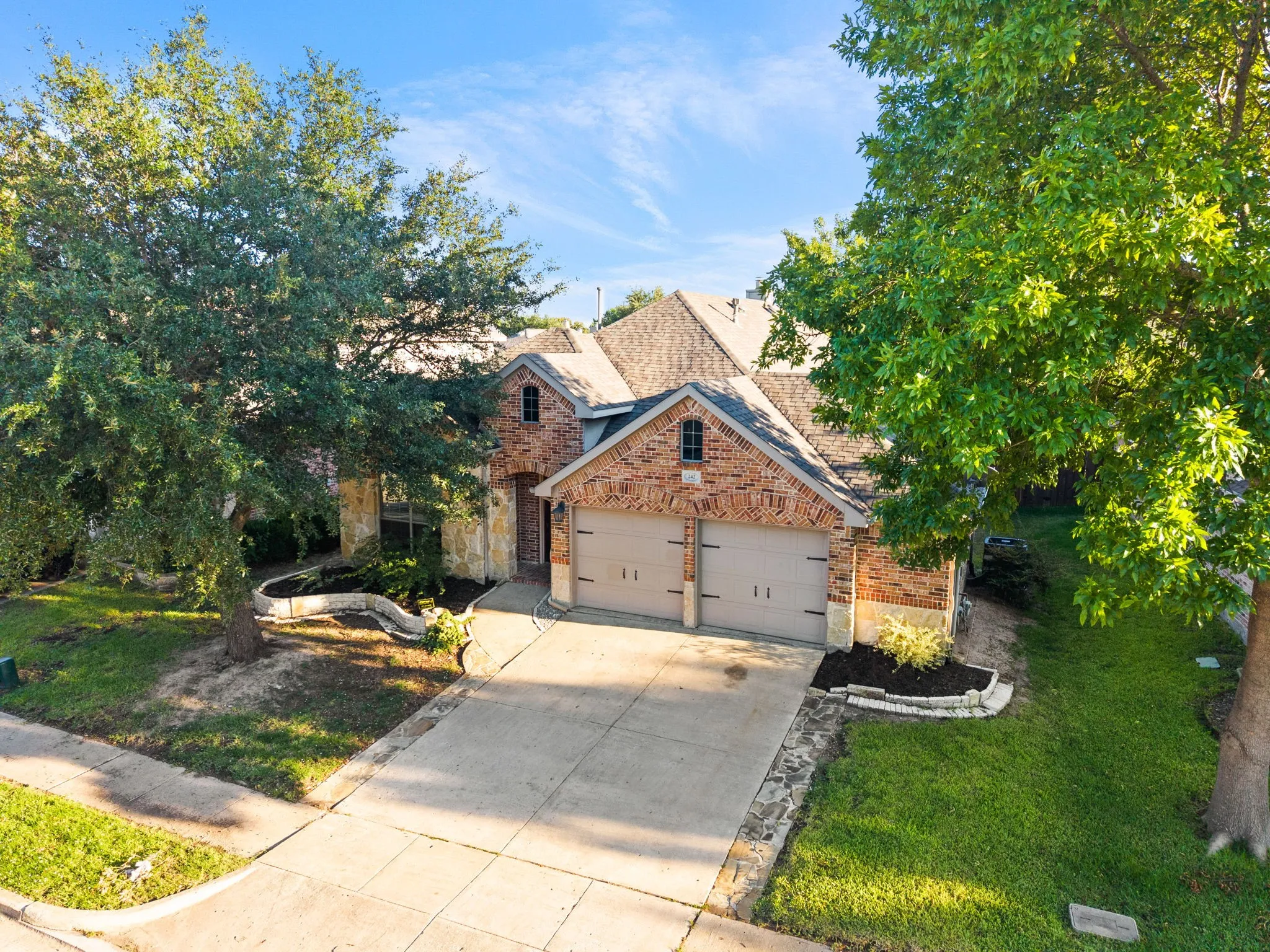 Elegant brick Colonial with a two-car garage featuring arched doors, situated on a landscaped lot with mature trees and a manicured lawn