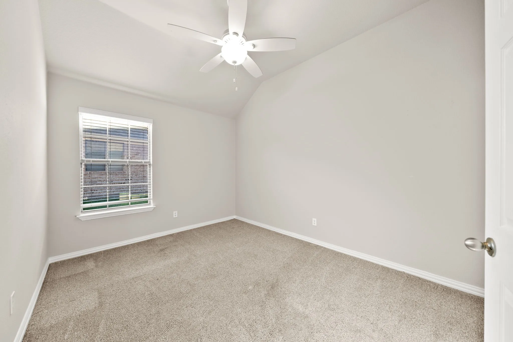 Vaulted ceiling, ceiling fan with integrated lighting, window with blinds, carpet flooring, and a paneled door