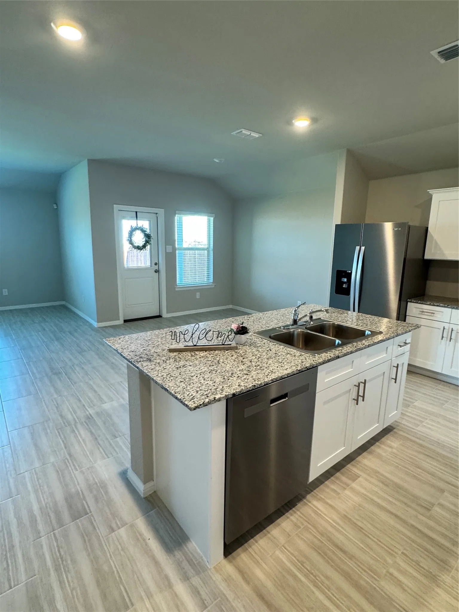 Kitchen with white cabinets, dishwasher, stainless steel fridge, a kitchen island with sink, and light wood-style floors