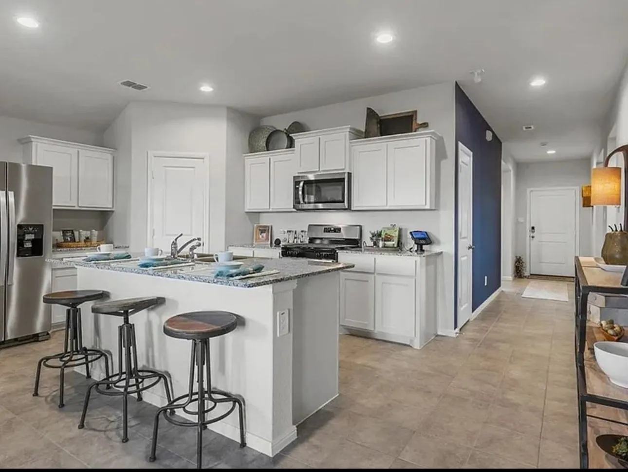 Staged Kitchen with a kitchen bar, stainless steel appliances, recessed lighting, white cabinets, and a kitchen island with sink. Hallway wall is not blue.