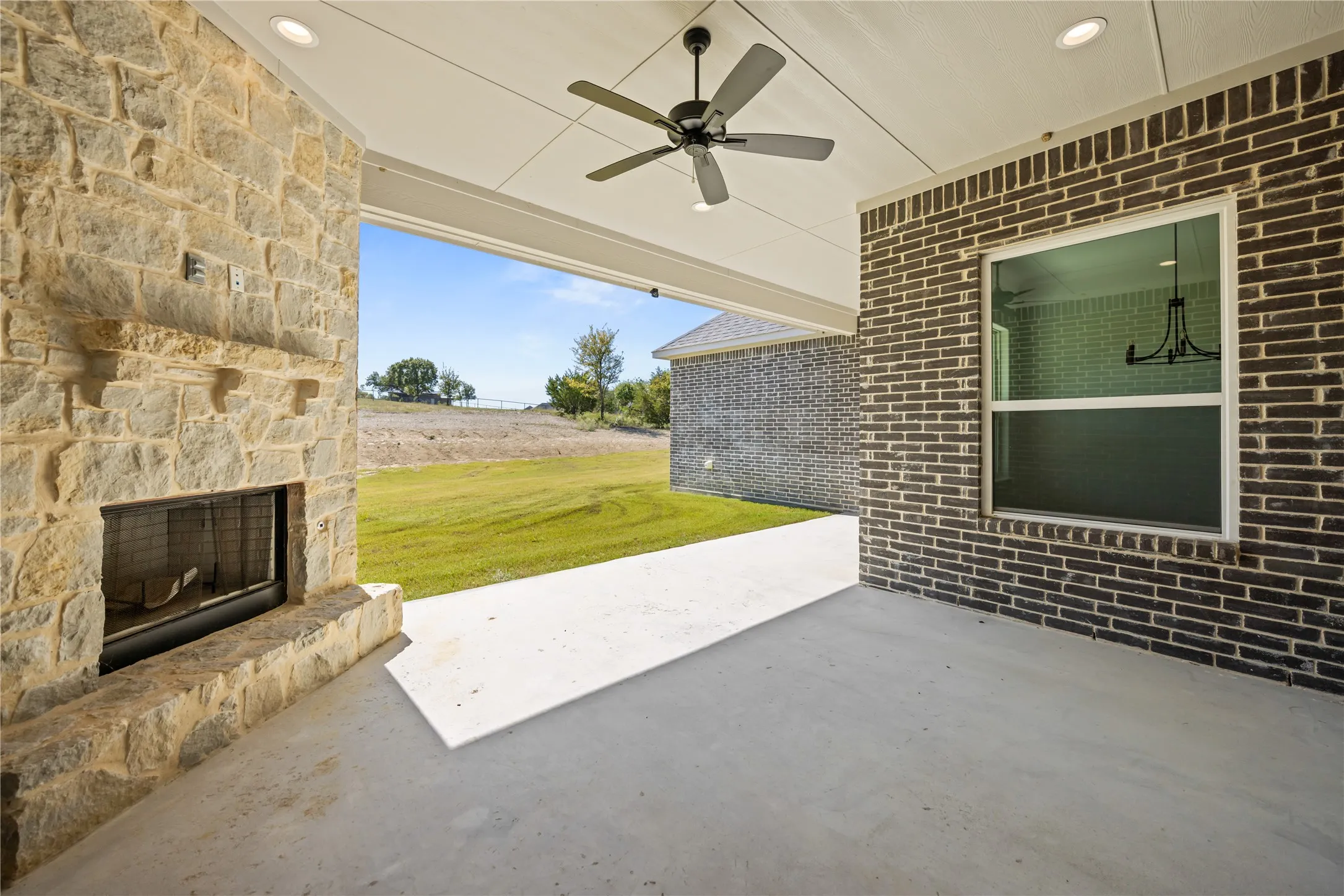 Covered outdoor patio featuring a stone fireplace, ceiling fan, recessed lighting, and expansive concrete flooring