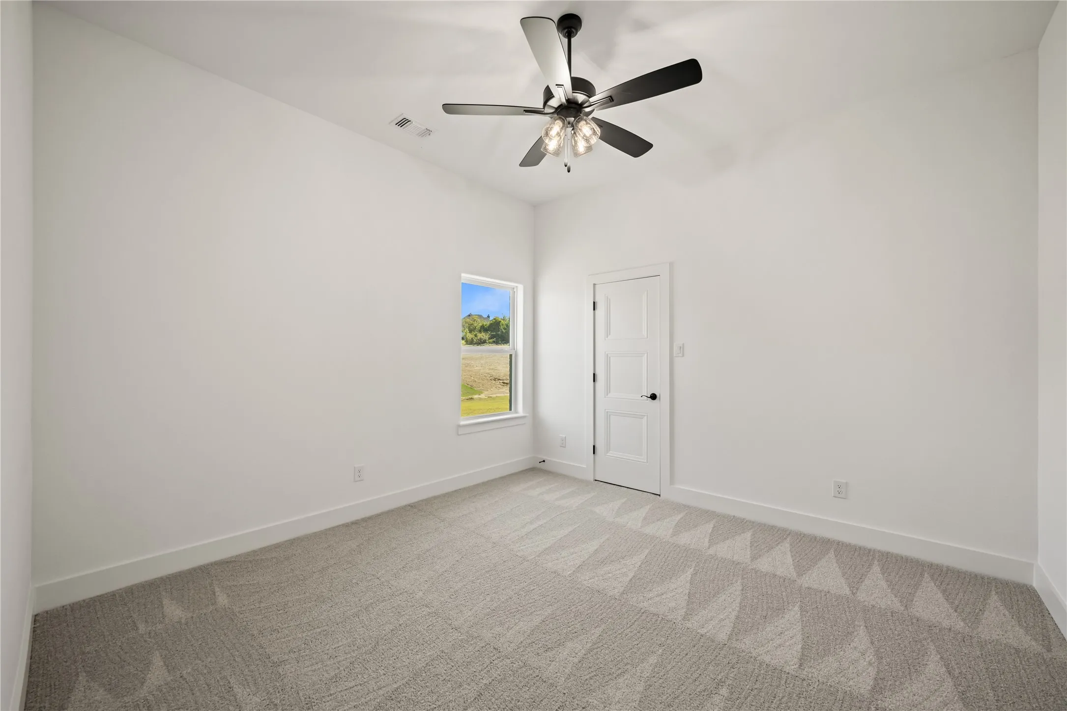 Neutral tone wall paint, patterned carpet flooring, white trim, single window, and a ceiling fan with light fixture