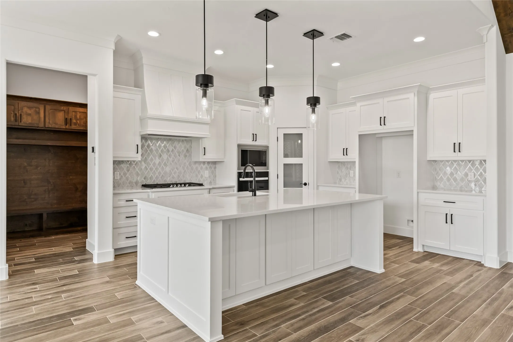 Spacious kitchen featuring an expansive center island with countertop seating, white shaker cabinetry, patterned tile backsplash, and wood-finish​​‌​​​​‌​​‌‌​‌‌​​​‌‌​‌​‌​‌​​​‌​​ flooring