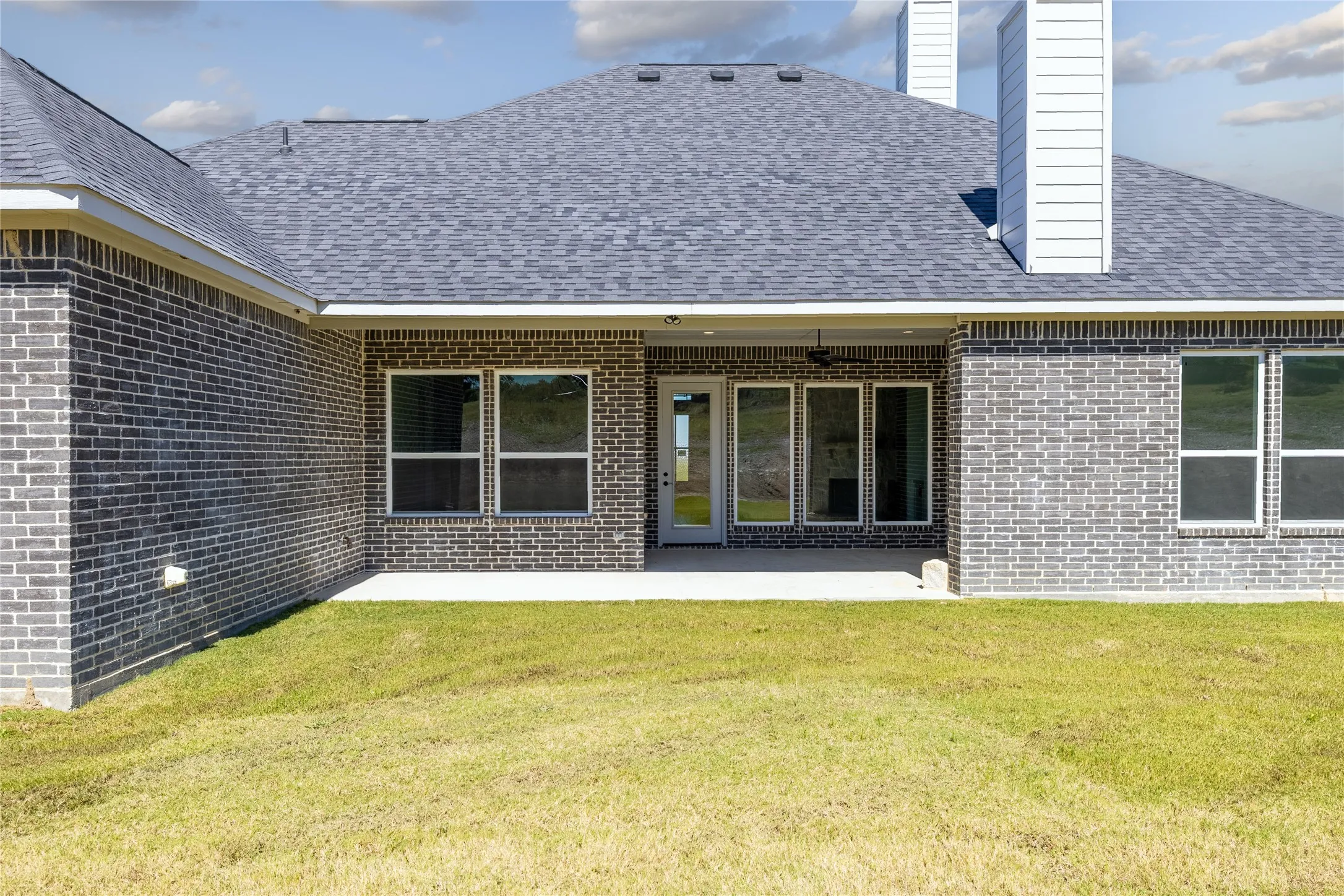 Brick exterior with a covered patio, multiple windows, and a glass-paneled door