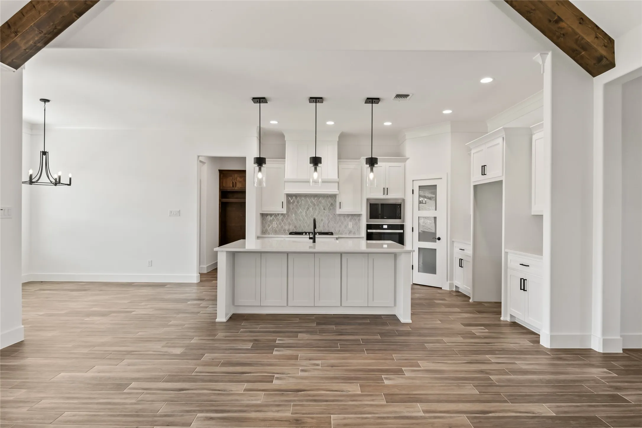 Spacious kitchen featuring an island with three pendant lights, white cabinetry, integrated oven, and a patterned tile backsplash