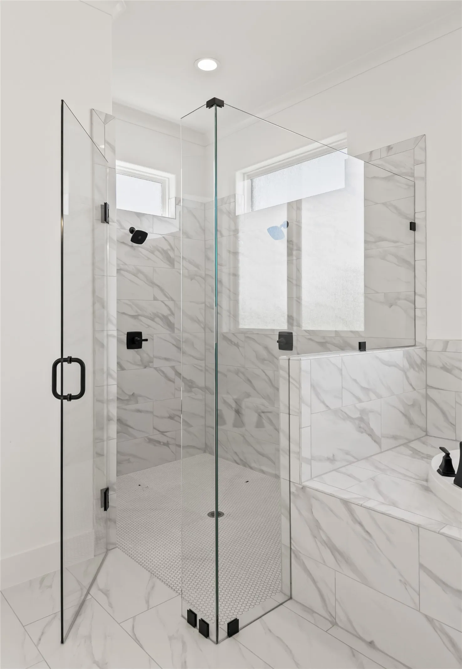 Walk-in glass shower with matte black hardware, white marble-look wall tile, and a white penny tile shower floor
