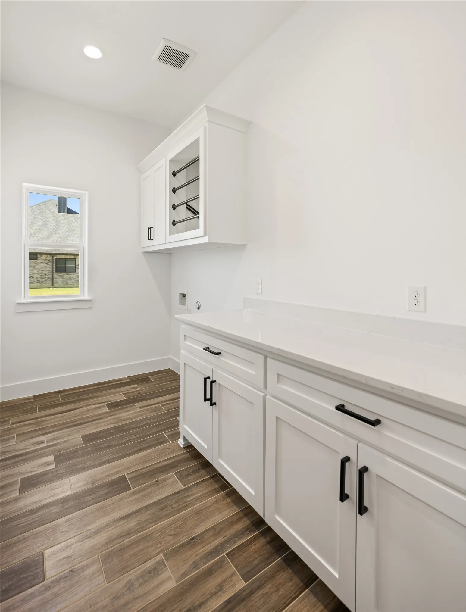 White shaker-style cabinetry with matte black hardware, white countertop, wood-finish flooring, and a built-in drying rack