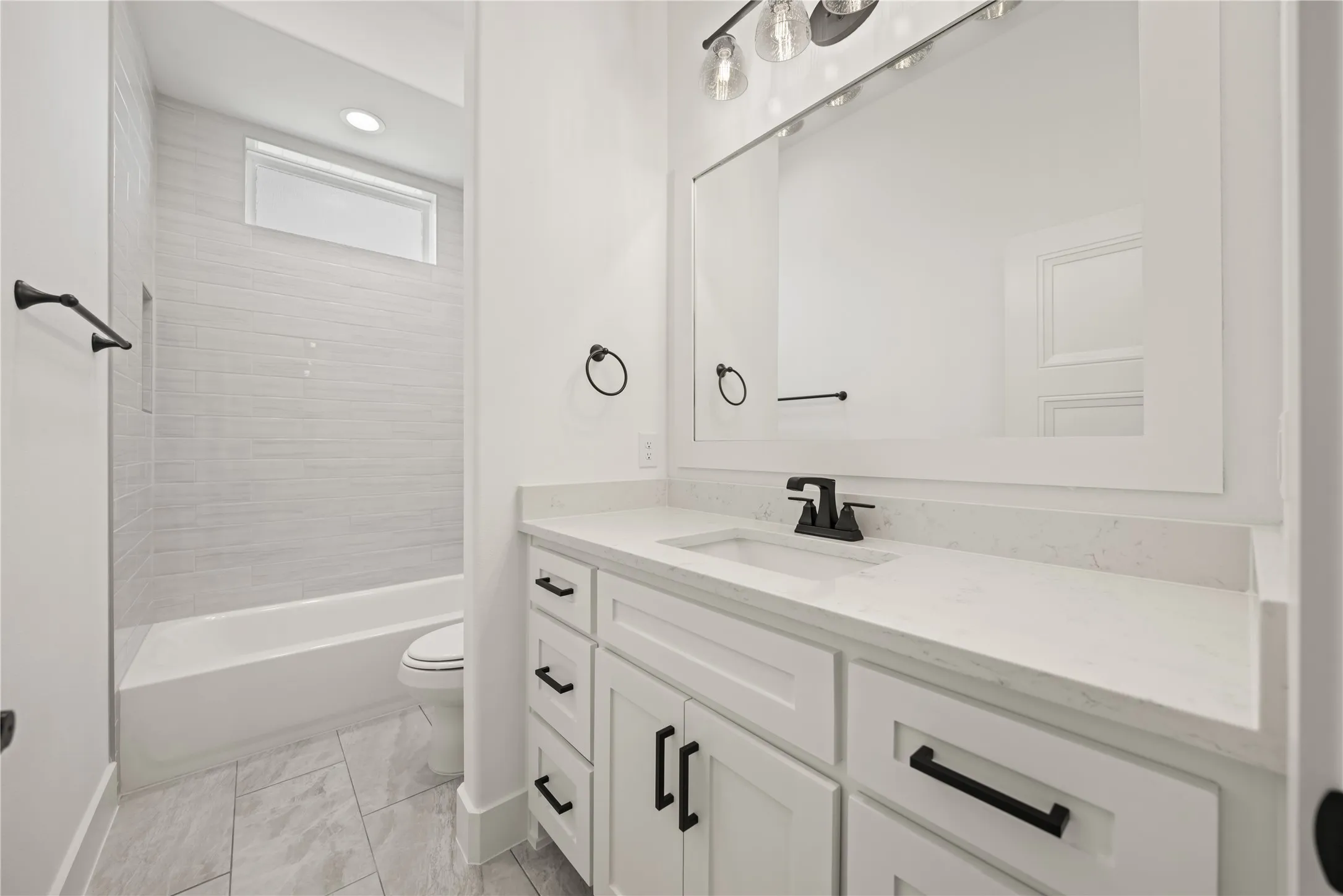 White shaker cabinetry with matte black hardware, white rectangular sink, light-toned countertop, and framed mirror