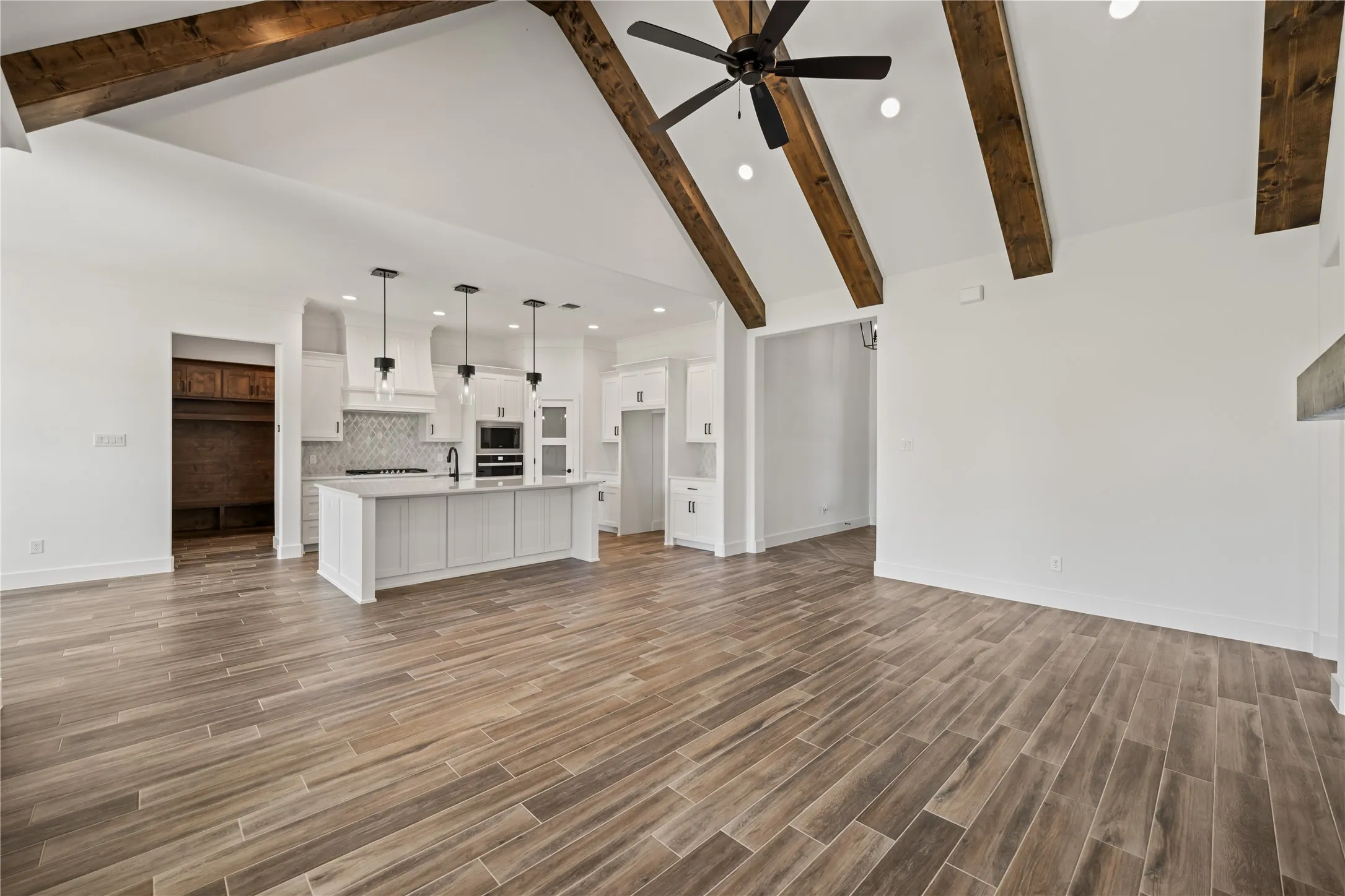 Vaulted ceilings with exposed beams, wood-finish flooring, recessed lighting, kitchen island with built-in sink, and pendant lighting