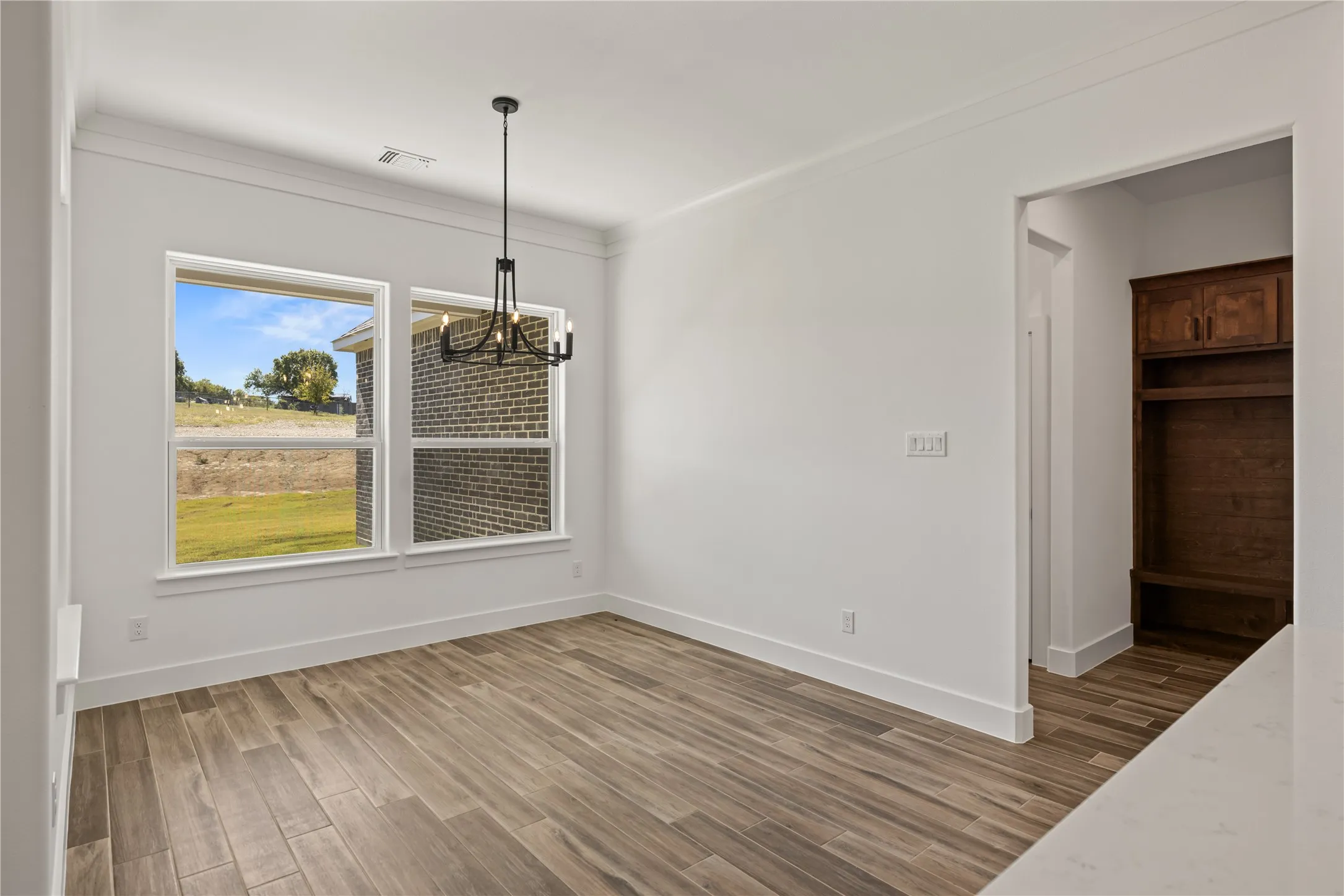 Spacious room featuring wood-finish flooring, large windows, a modern chandelier, and crown molding