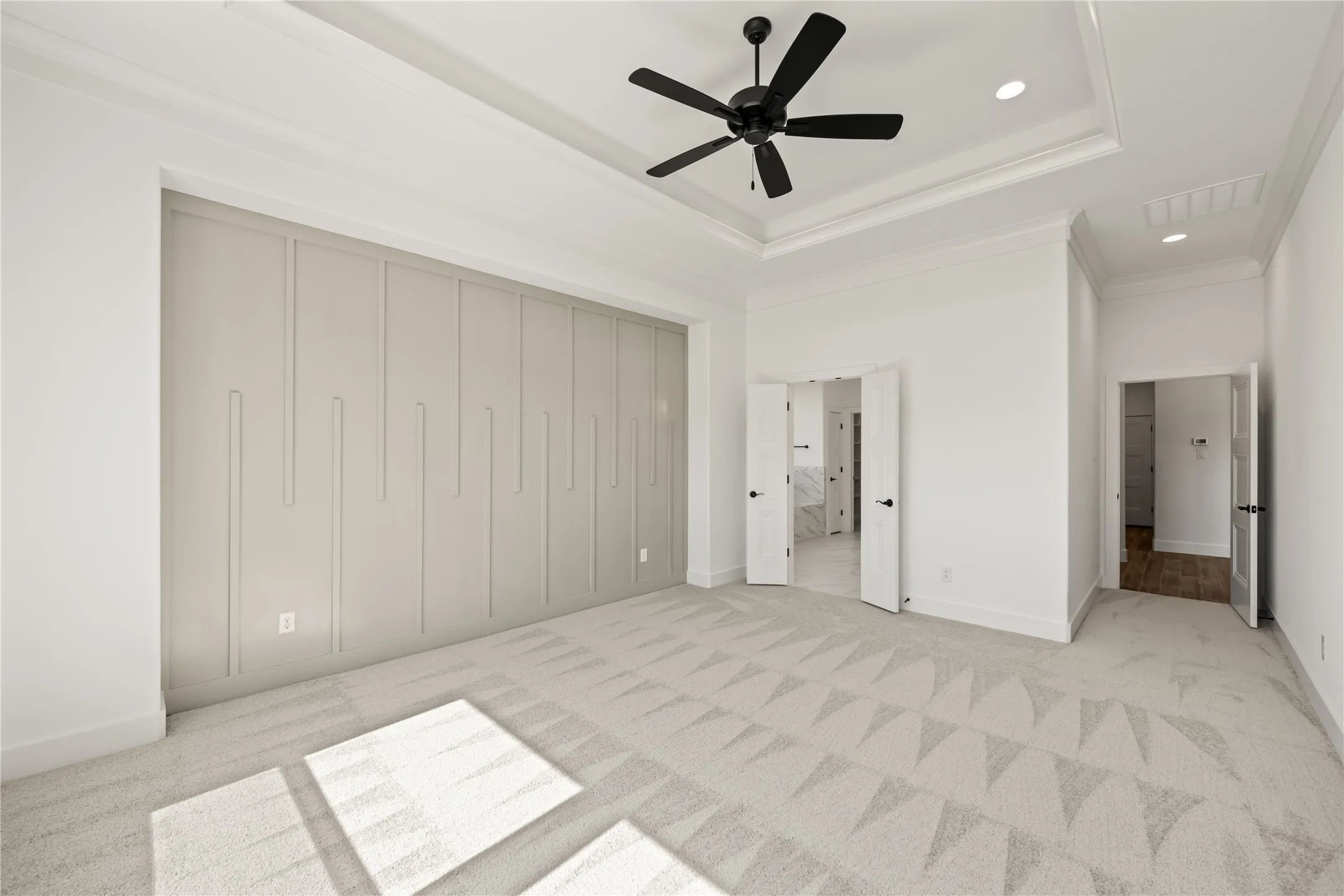 Tray ceiling with recessed lighting and a ceiling fan, geometric pattern accent wall, and patterned carpet flooring
