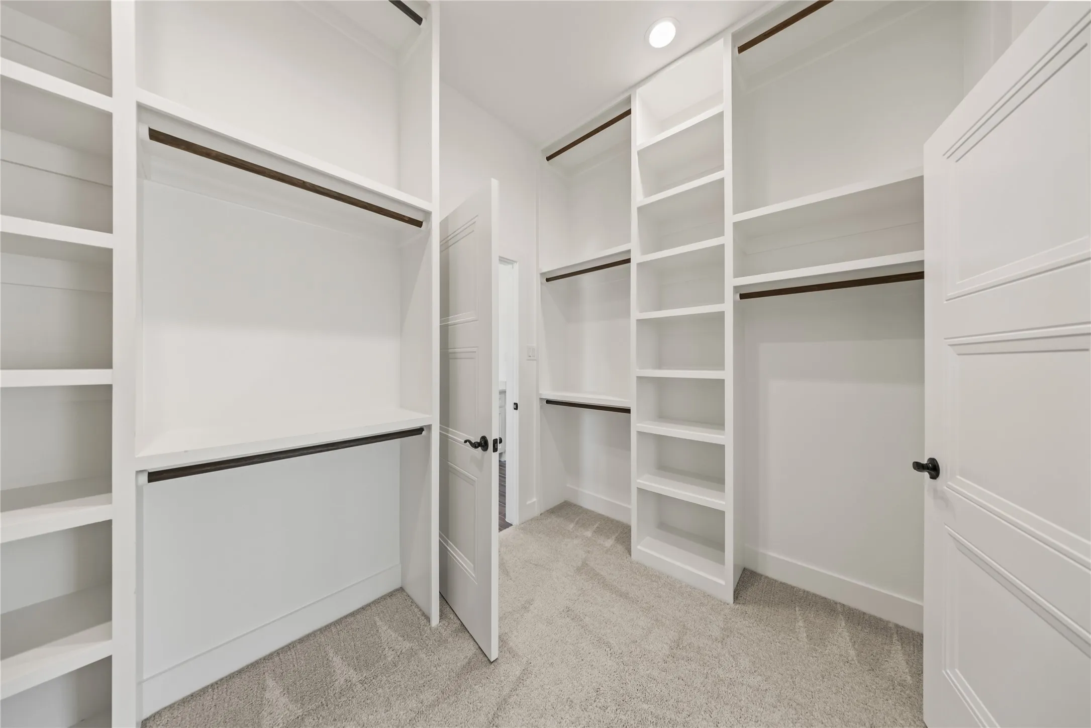 Built-in shelving, white cabinetry, integrated hanging rods, recessed lighting, and carpeted flooring