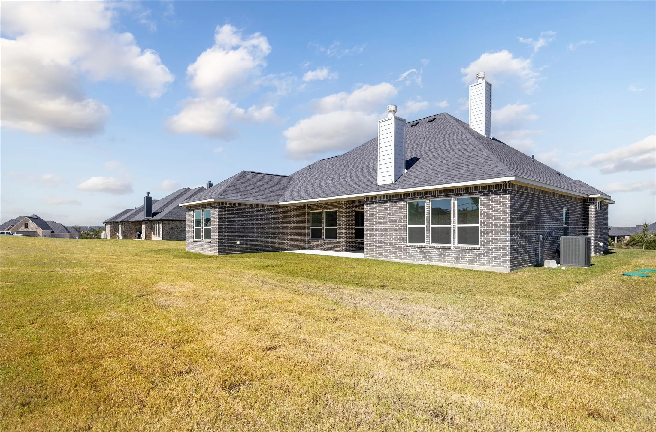 Exterior featuring brick siding, a dark shingle roof, multiple windows, and two chimney stacks