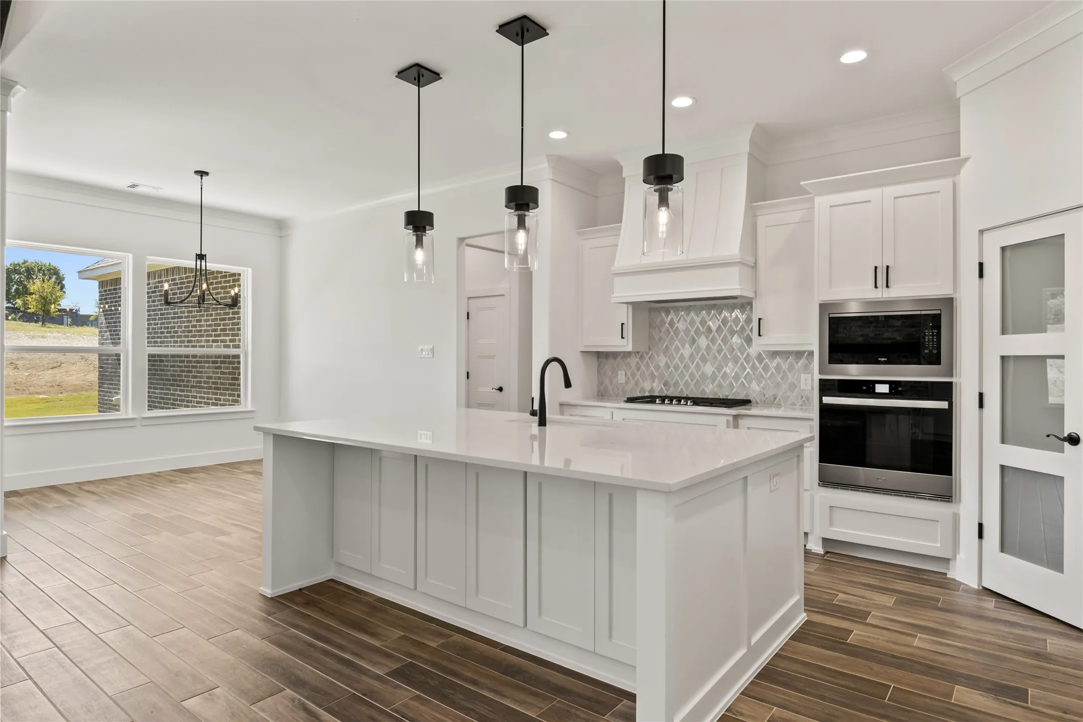 White kitchen featuring an island with a light-colored countertop, built-in stainless steel appliances, and wood-finish flooring